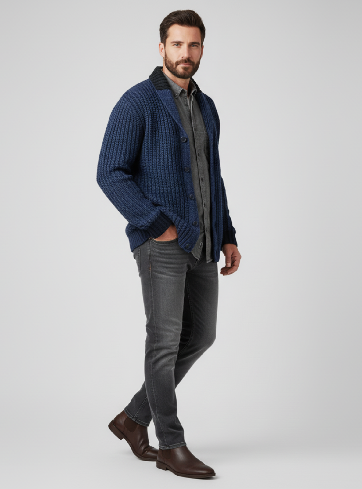 Man wearing a blue ribbed sweater, gray shirt, gray jeans, and brown shoes on a white background
