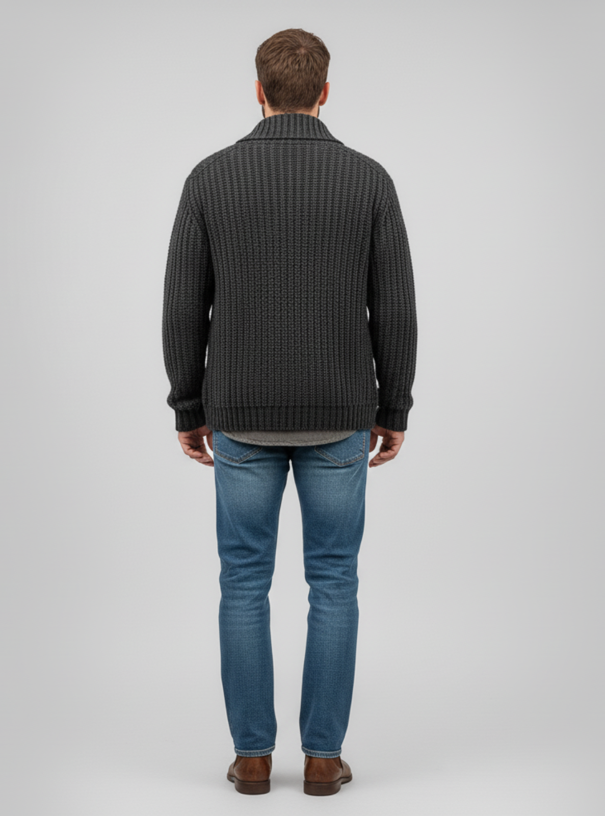 Man wearing a dark gray sweater and blue jeans on a light gray background