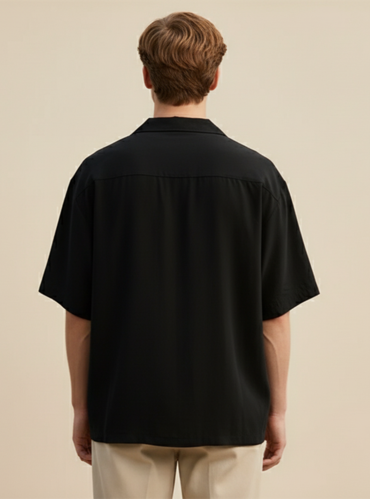 Man wearing a black shirt and beige pants against a beige background