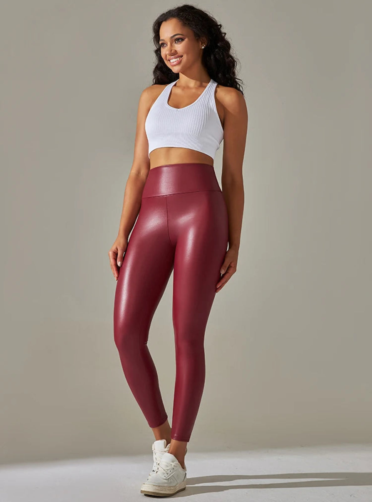 Woman wearing maroon leggings and a white crop top on a neutral background