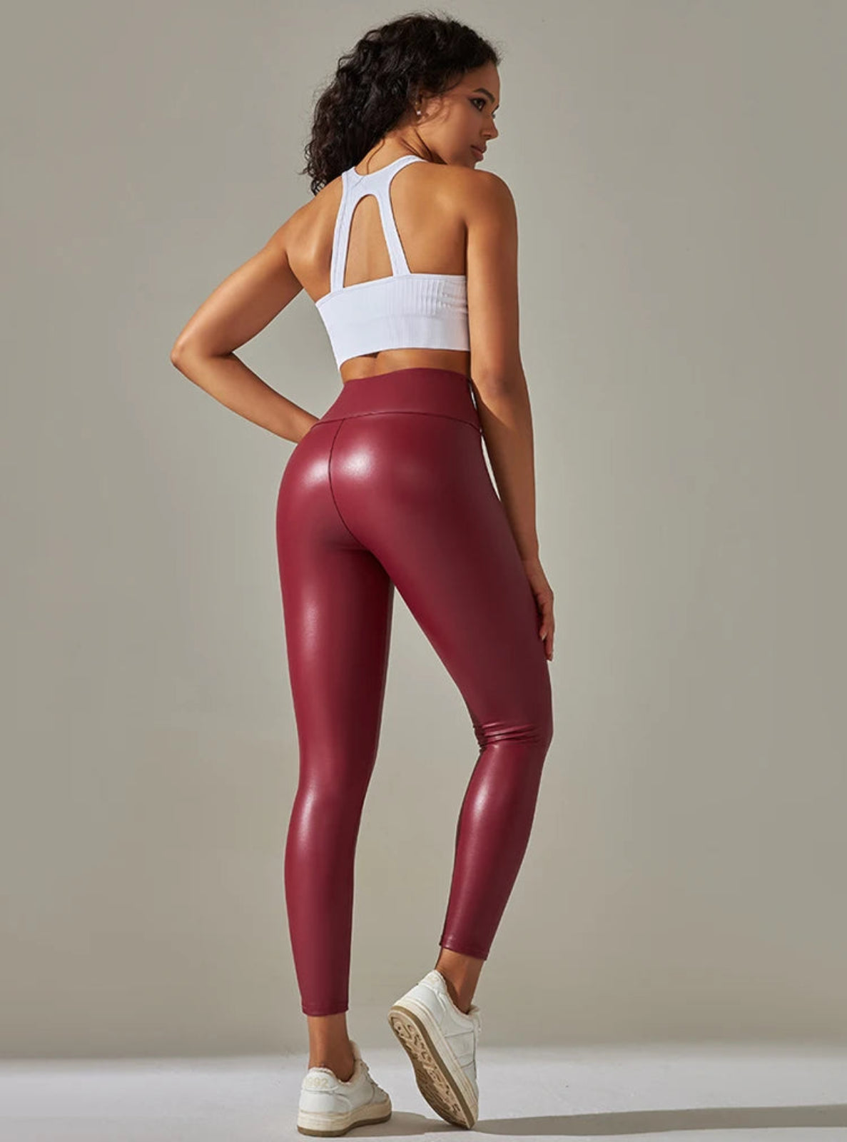 Woman wearing maroon leggings and a white sports bra against a neutral background