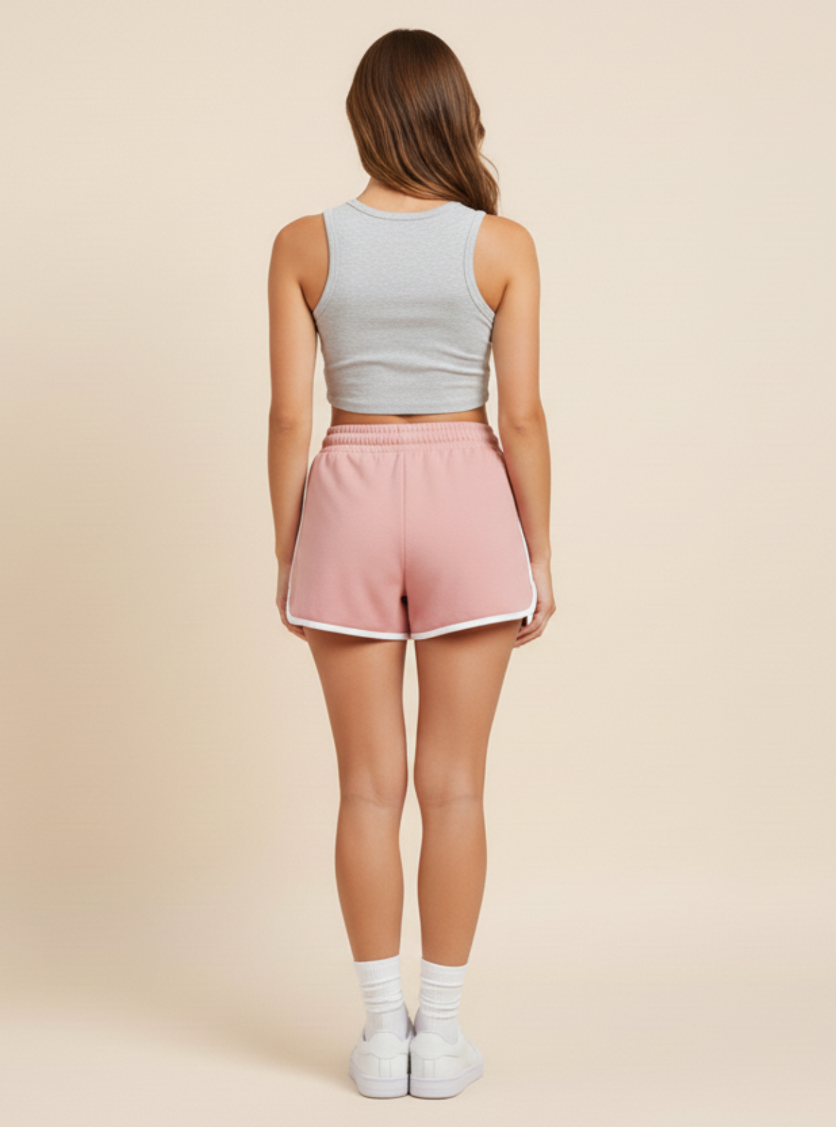 Woman wearing a light gray crop top and pink shorts on a beige background