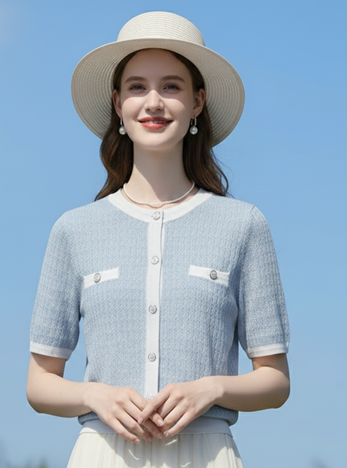 Woman wearing a light blue cardigan and white hat against a clear blue sky
