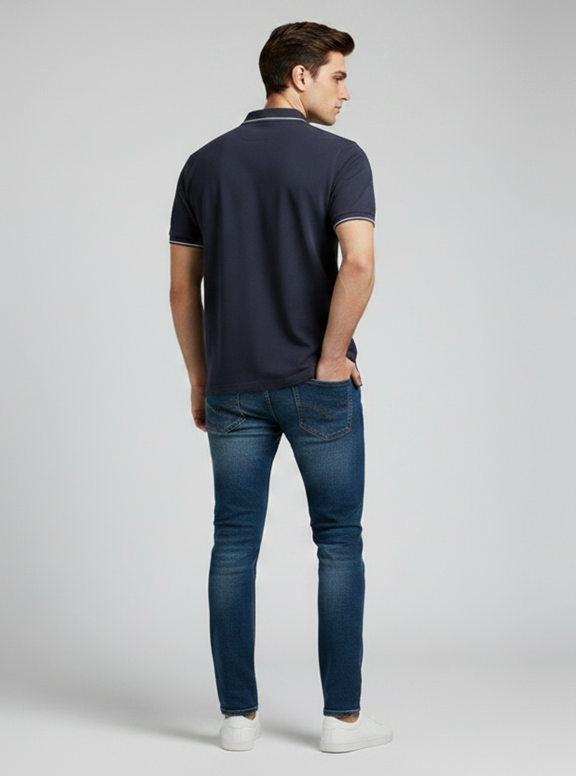 Man wearing a navy polo shirt and blue jeans on a gray background