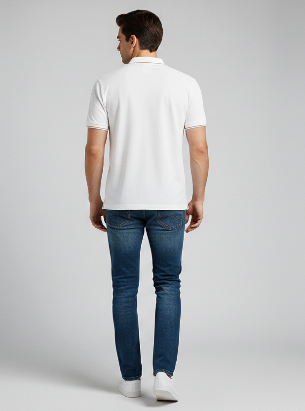 Man wearing a white polo shirt and blue jeans on a gray background
