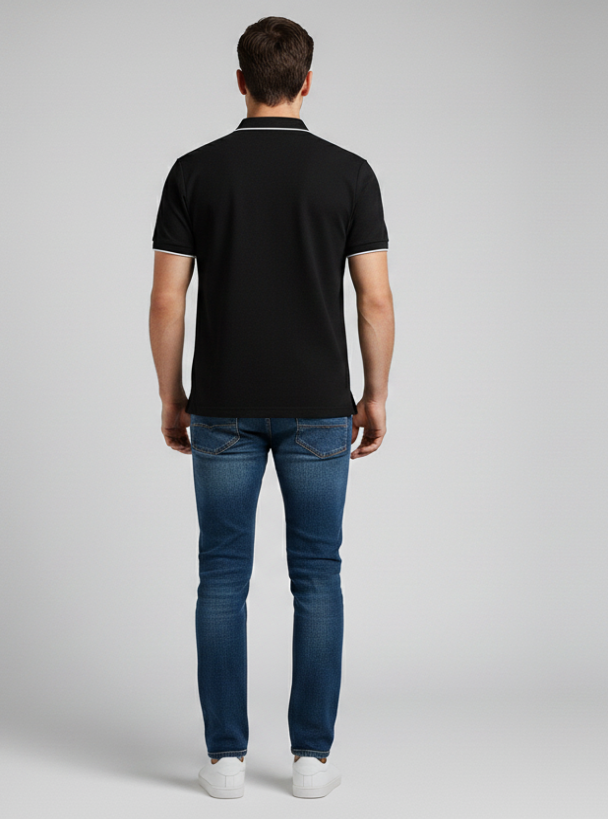 Man wearing a black polo shirt and blue jeans on a gray background
