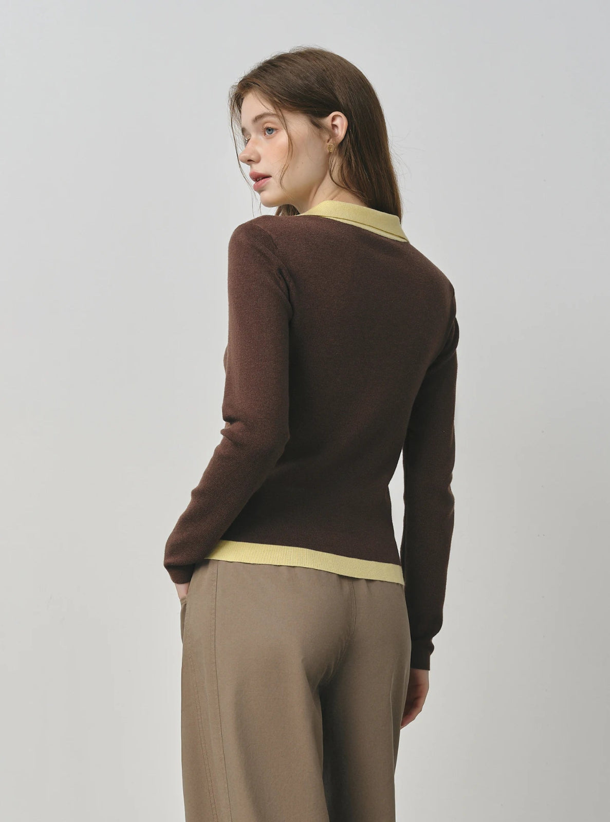 Woman wearing a brown sweater with  yellow trim on a plain background