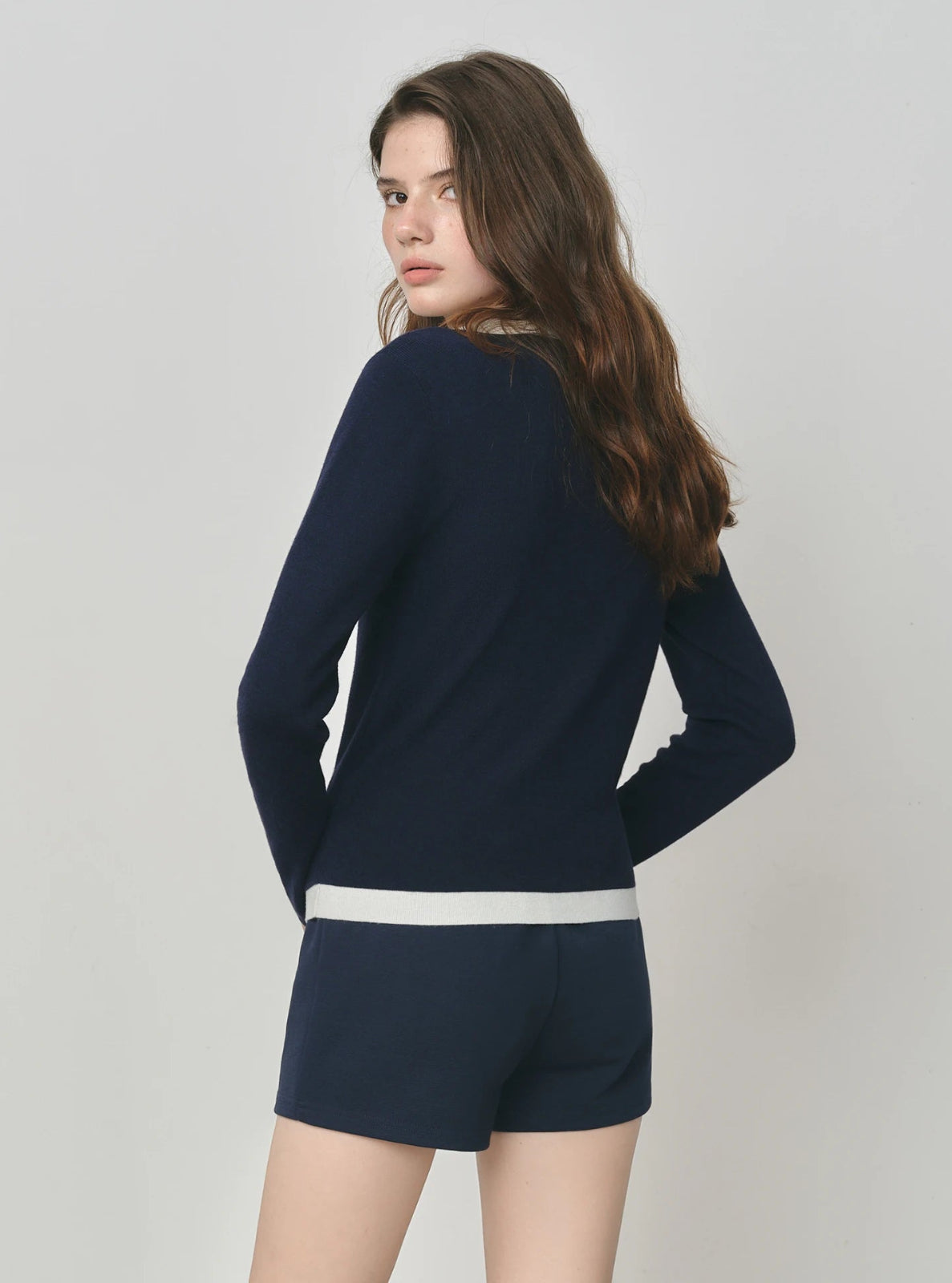 Woman wearing a navy blue outfit with white trim on a plain background