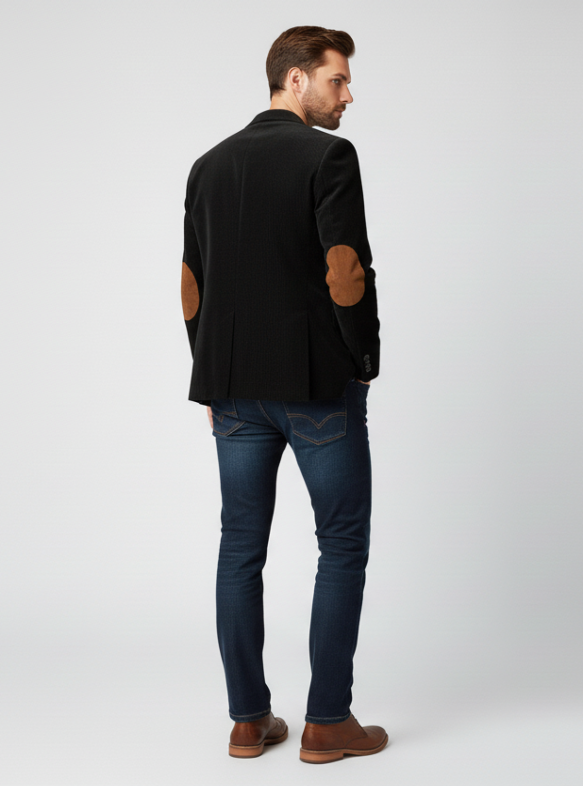Man wearing a black blazer, blue jeans, and brown shoes on a white background