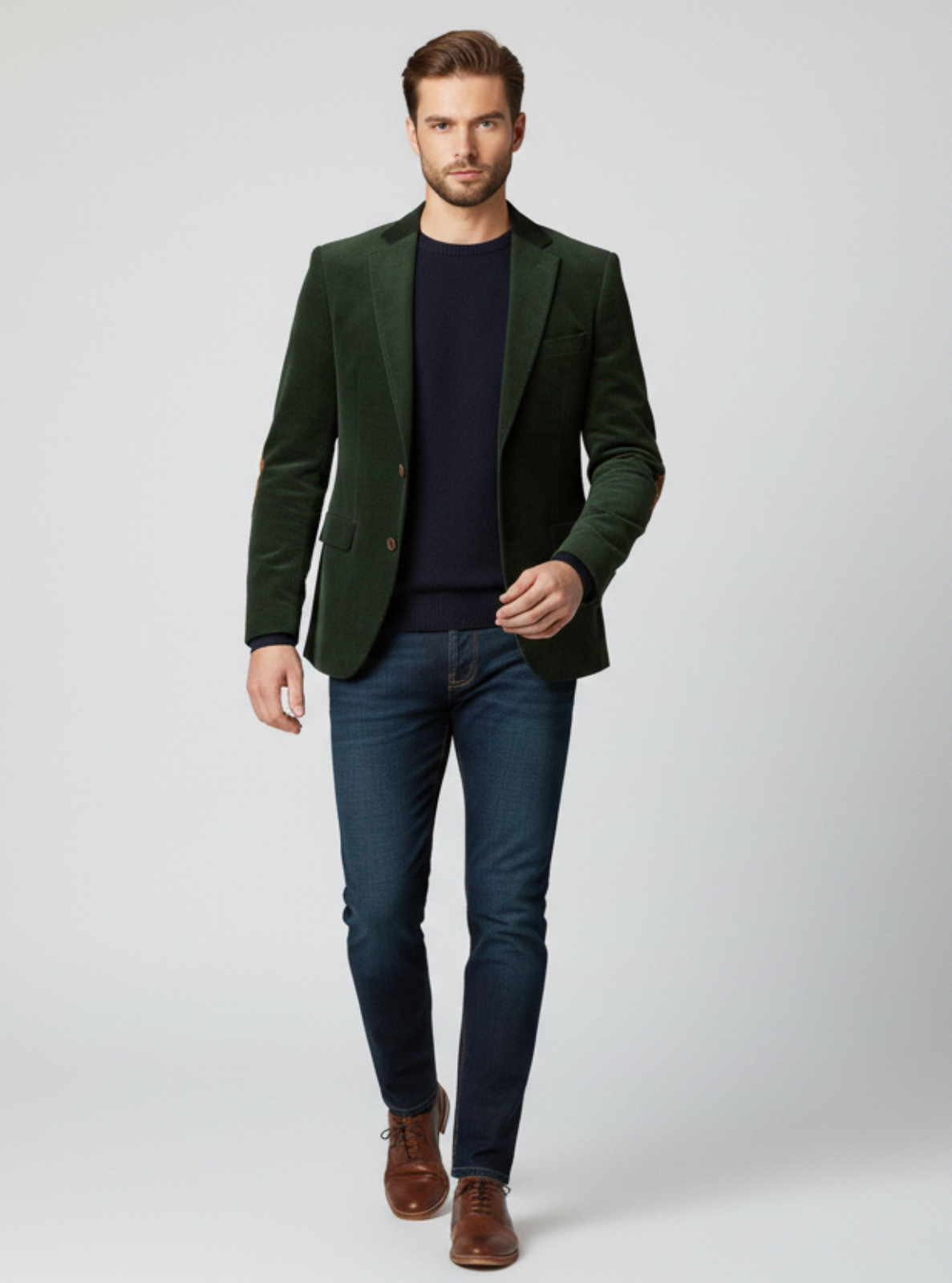 Man wearing a green blazer, navy shirt, blue jeans, and brown shoes on a white background