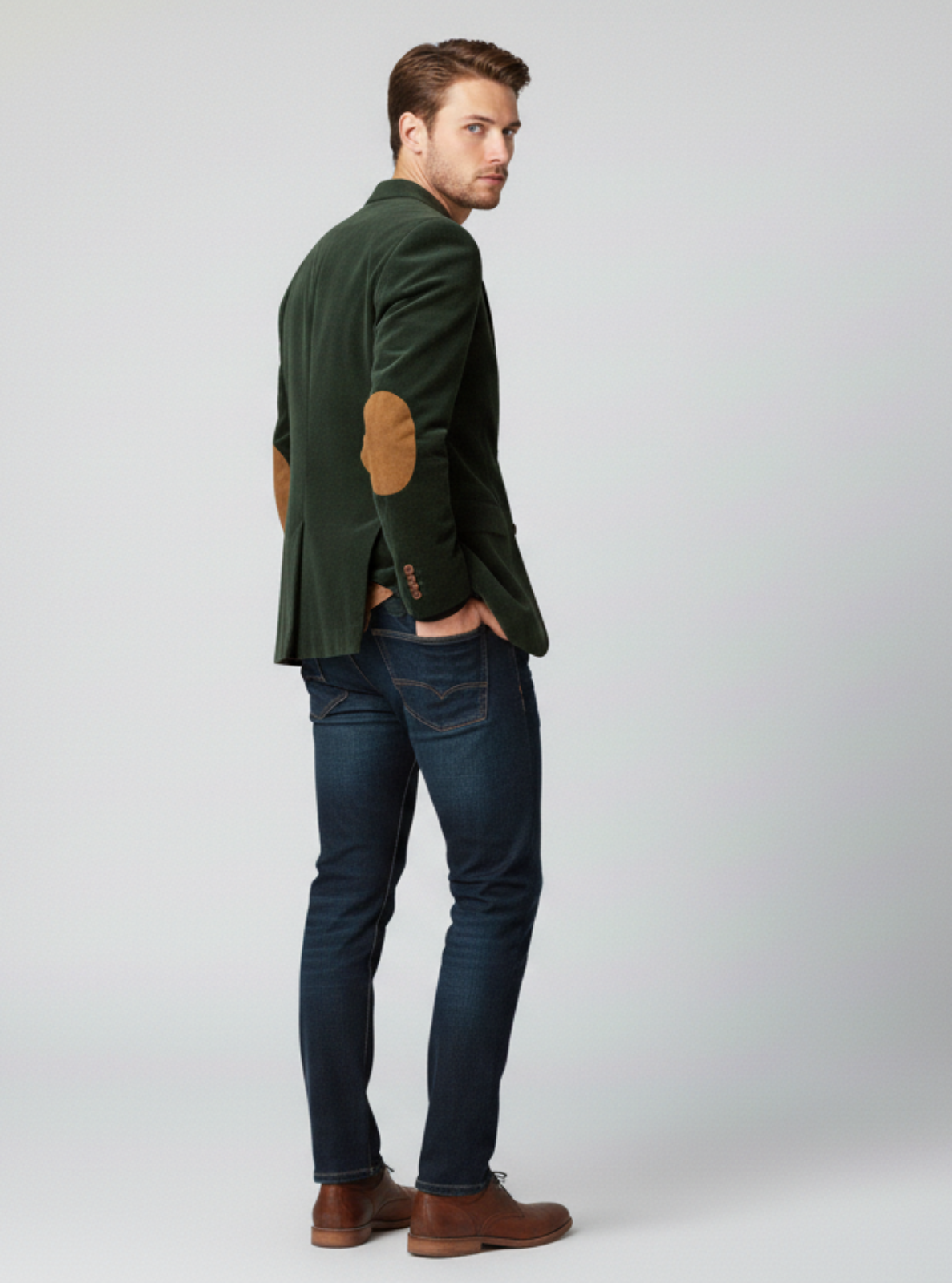 Man wearing a green jacket with brown accents, blue jeans, and brown shoes on a white background