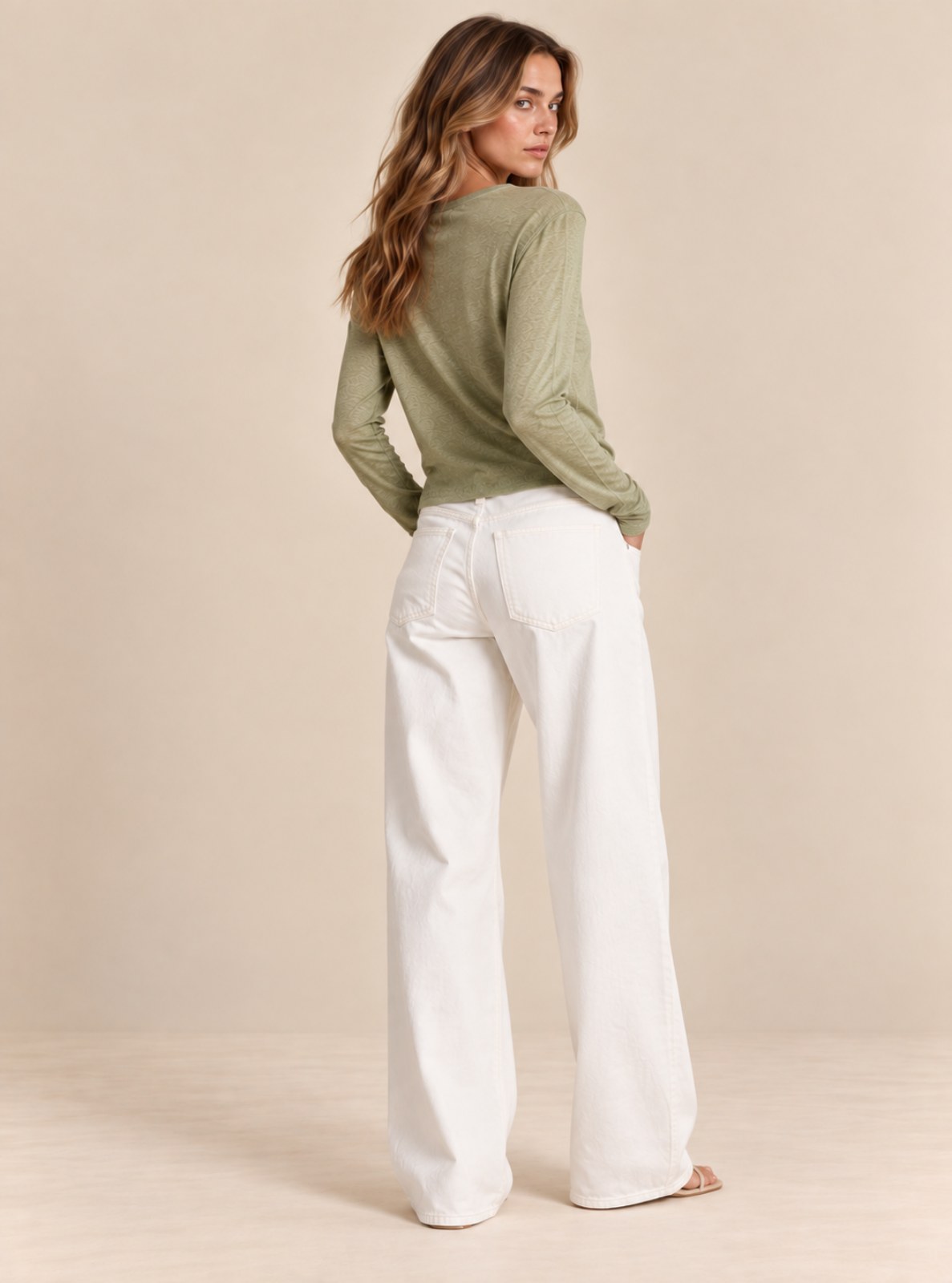 A woman shown from the back wearing an olive green ribbed long-sleeve top and white wide-leg jeans, standing against a plain beige studio backdrop.