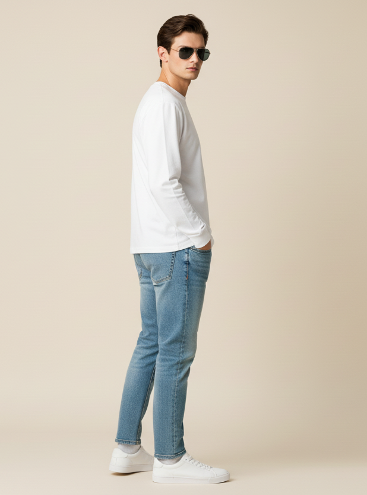 Man wearing a white long-sleeve shirt, blue jeans, and sunglasses on a beige background