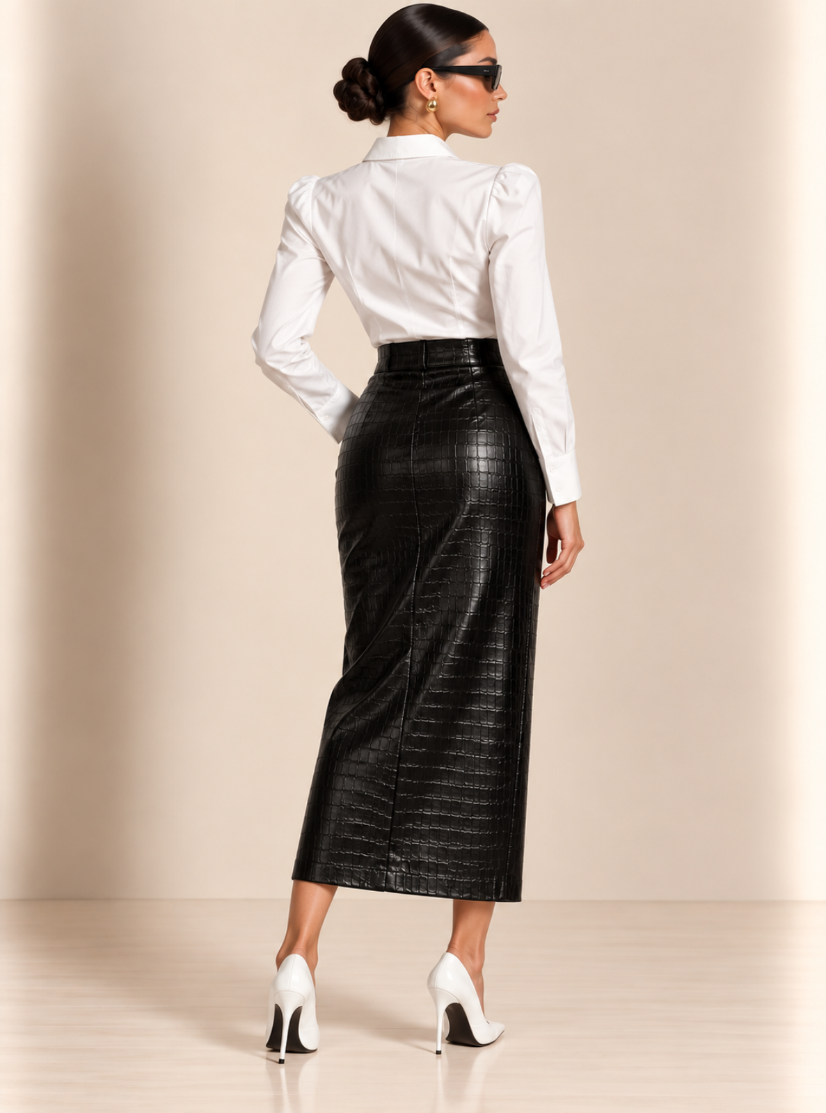 A woman shown from the back wearing a white long-sleeve blouse and a black textured faux-croc midi skirt, paired with white high heels, against a warm beige studio backdrop.