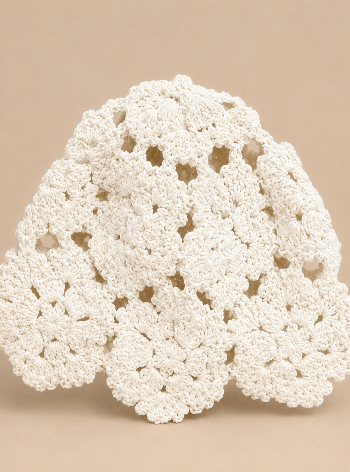 An off-white crocheted doily with a scalloped, lace-like pattern, displayed against a solid beige background.