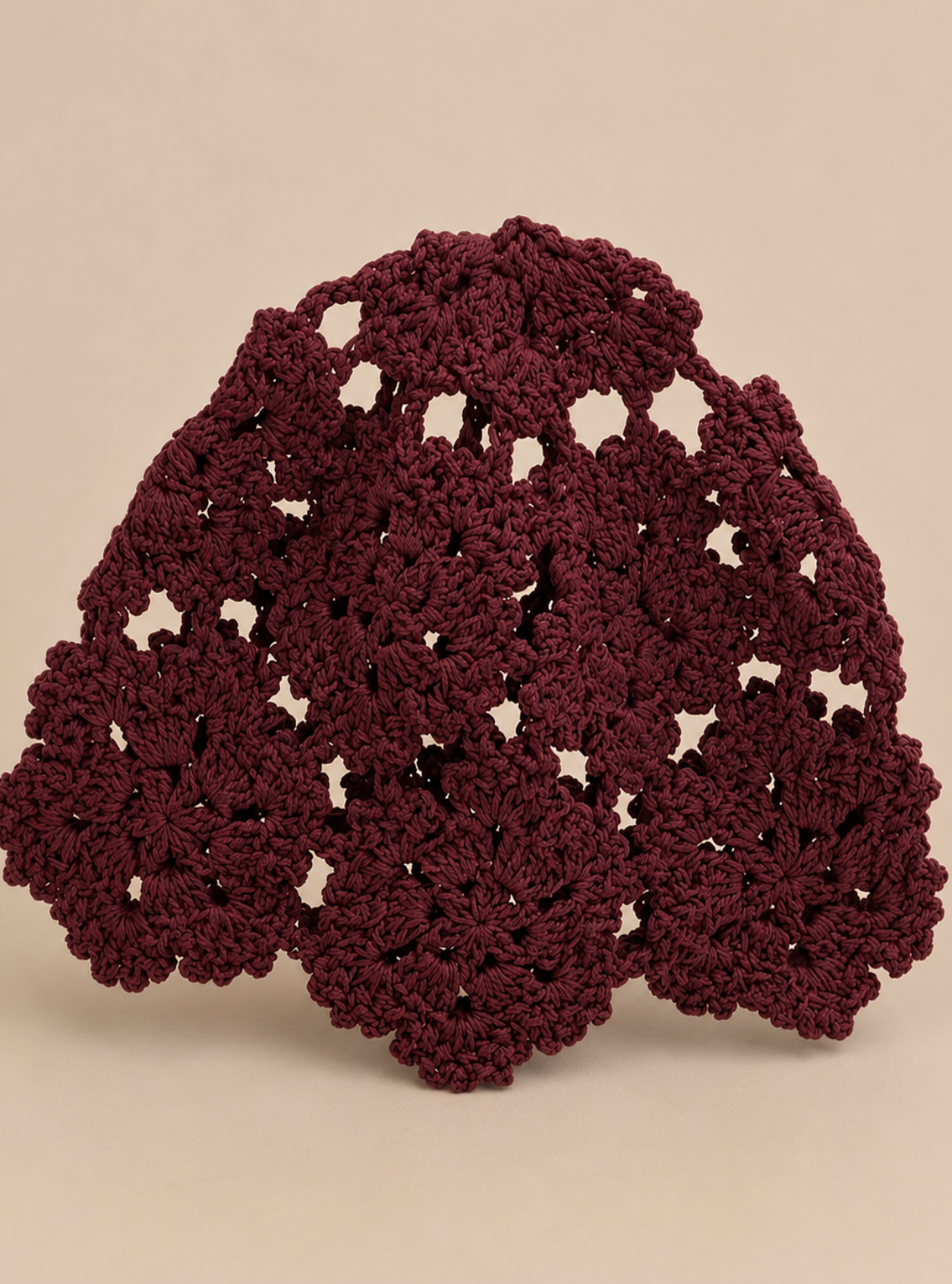 A handmade, scalloped crocheted headband in a deep burgundy color, displayed against a solid beige background.