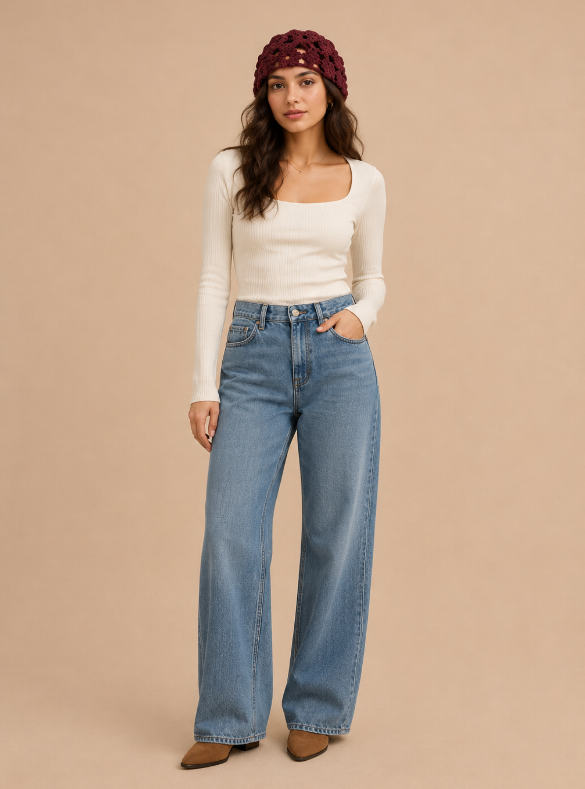 A woman modeling a pair of light-wash wide-leg blue jeans with a white long-sleeve top and a burgundy knit headband, standing against a solid beige studio background.