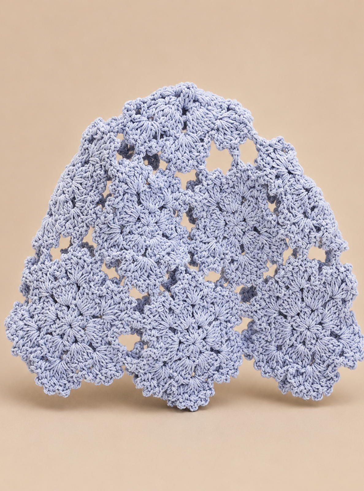 A light blue crocheted lace doily with a scalloped edge, displayed on a solid beige background.