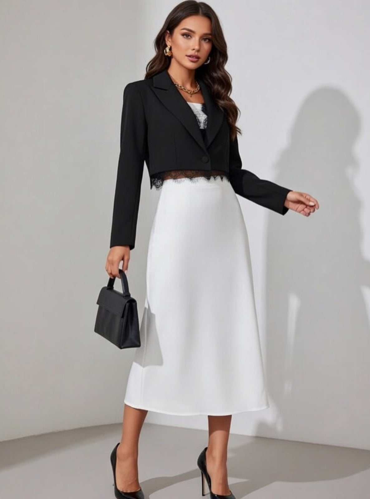 Woman wearing a black blazer and white skirt with a black handbag against a plain background
