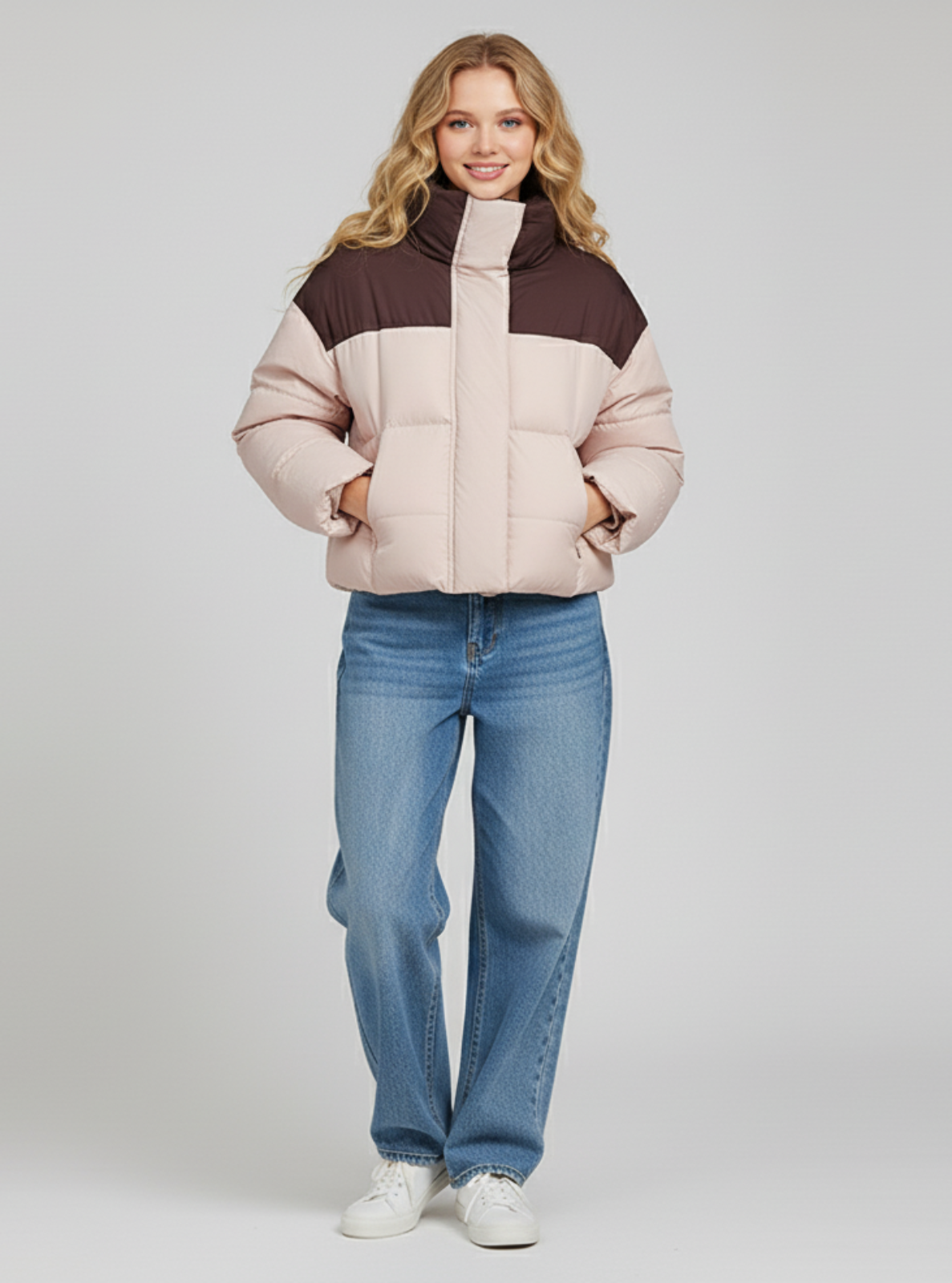 Woman wearing a two-tone puffer jacket and blue jeans on a plain background