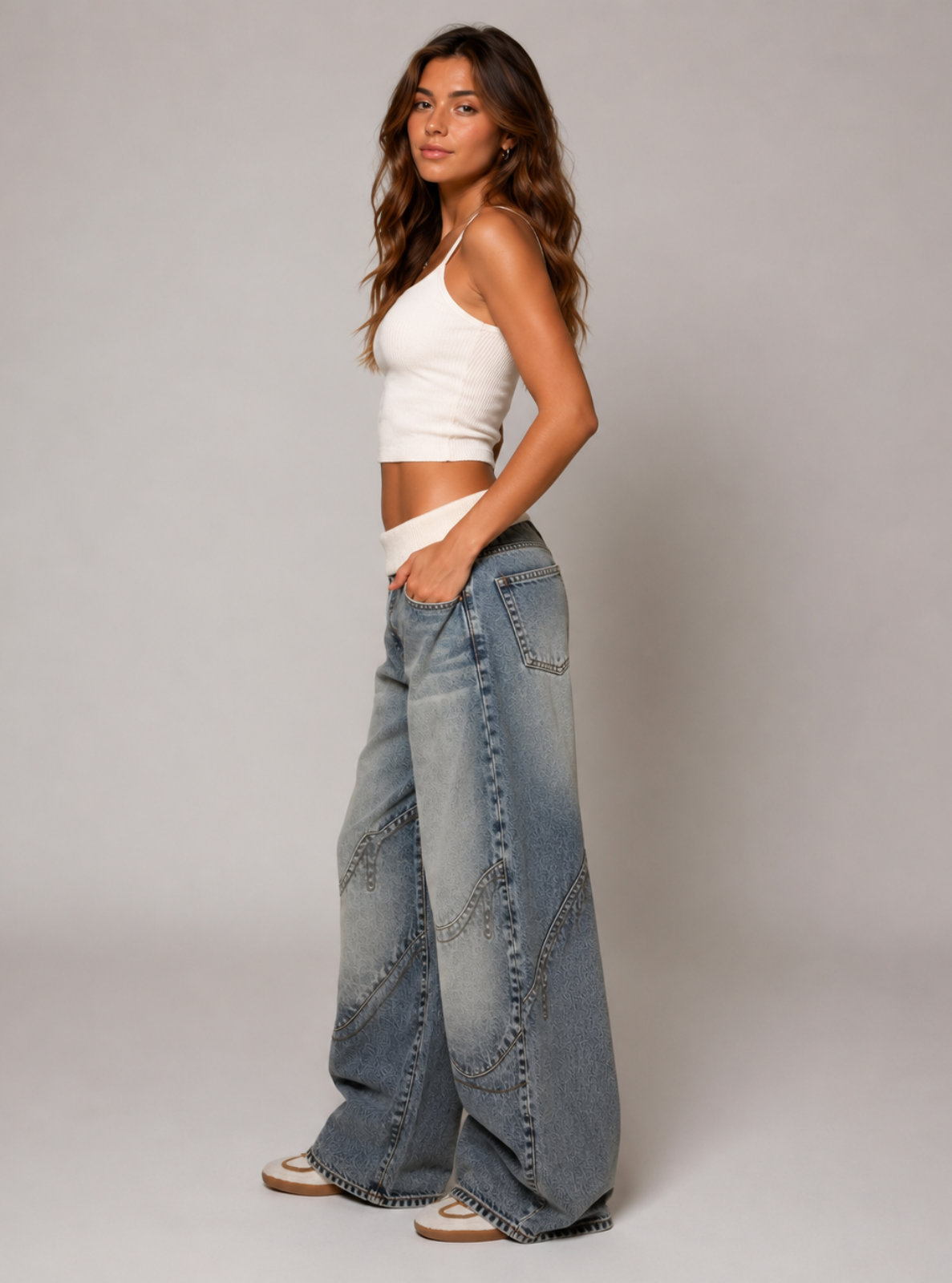 Woman wearing a white crop top and blue jeans on a plain background
