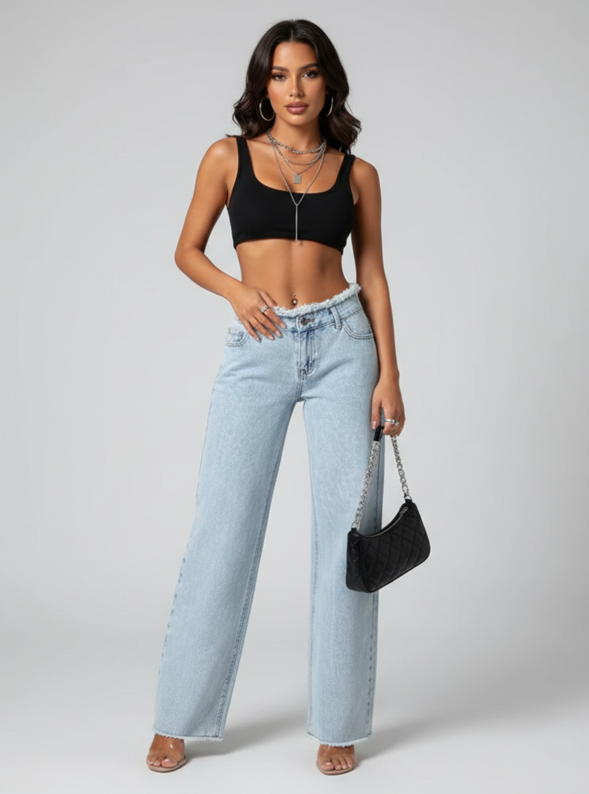 Woman wearing a black crop top and light blue jeans, holding a black handbag on a gray background