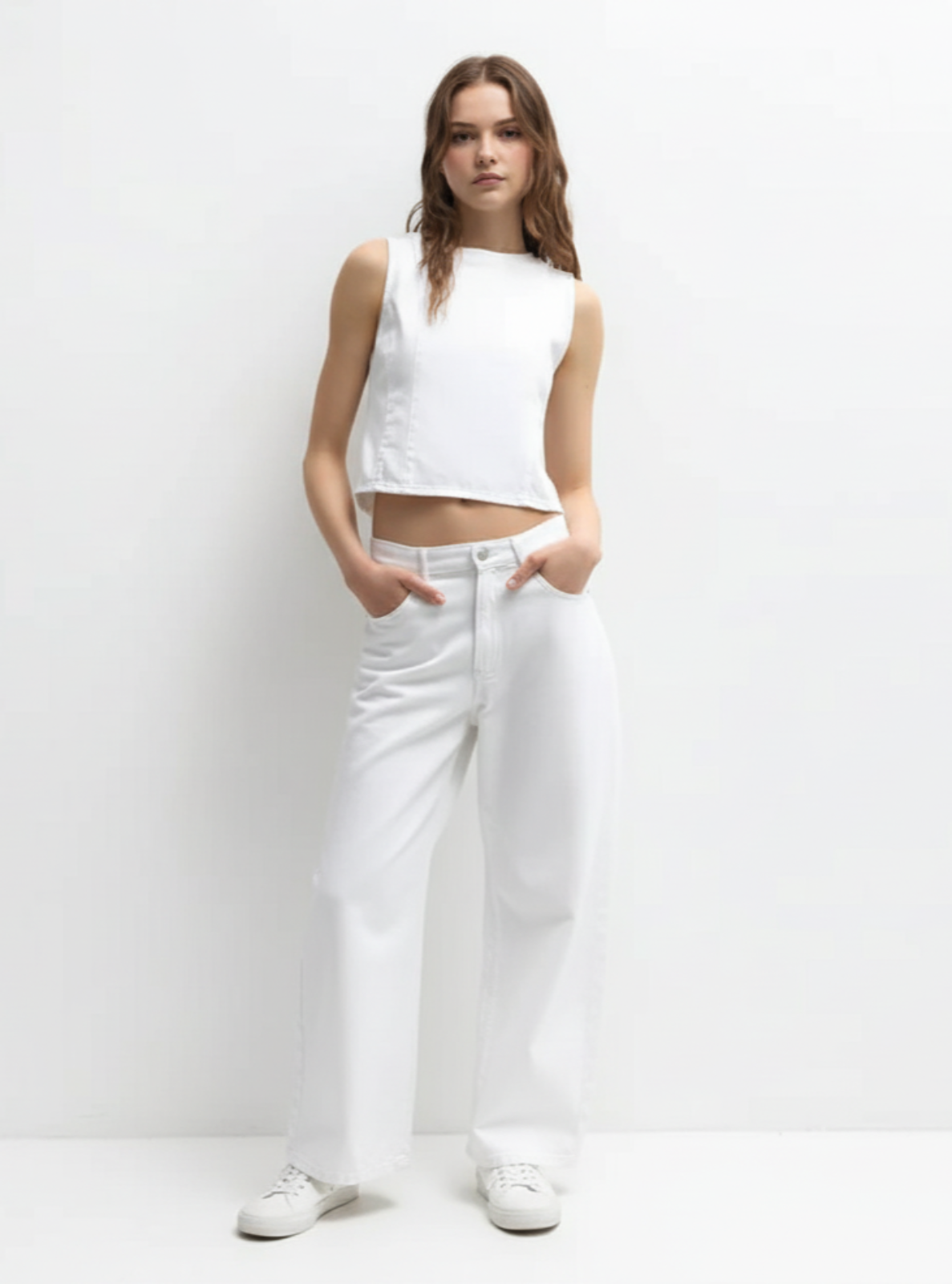 Woman wearing a white sleeveless top and white pants against a plain background