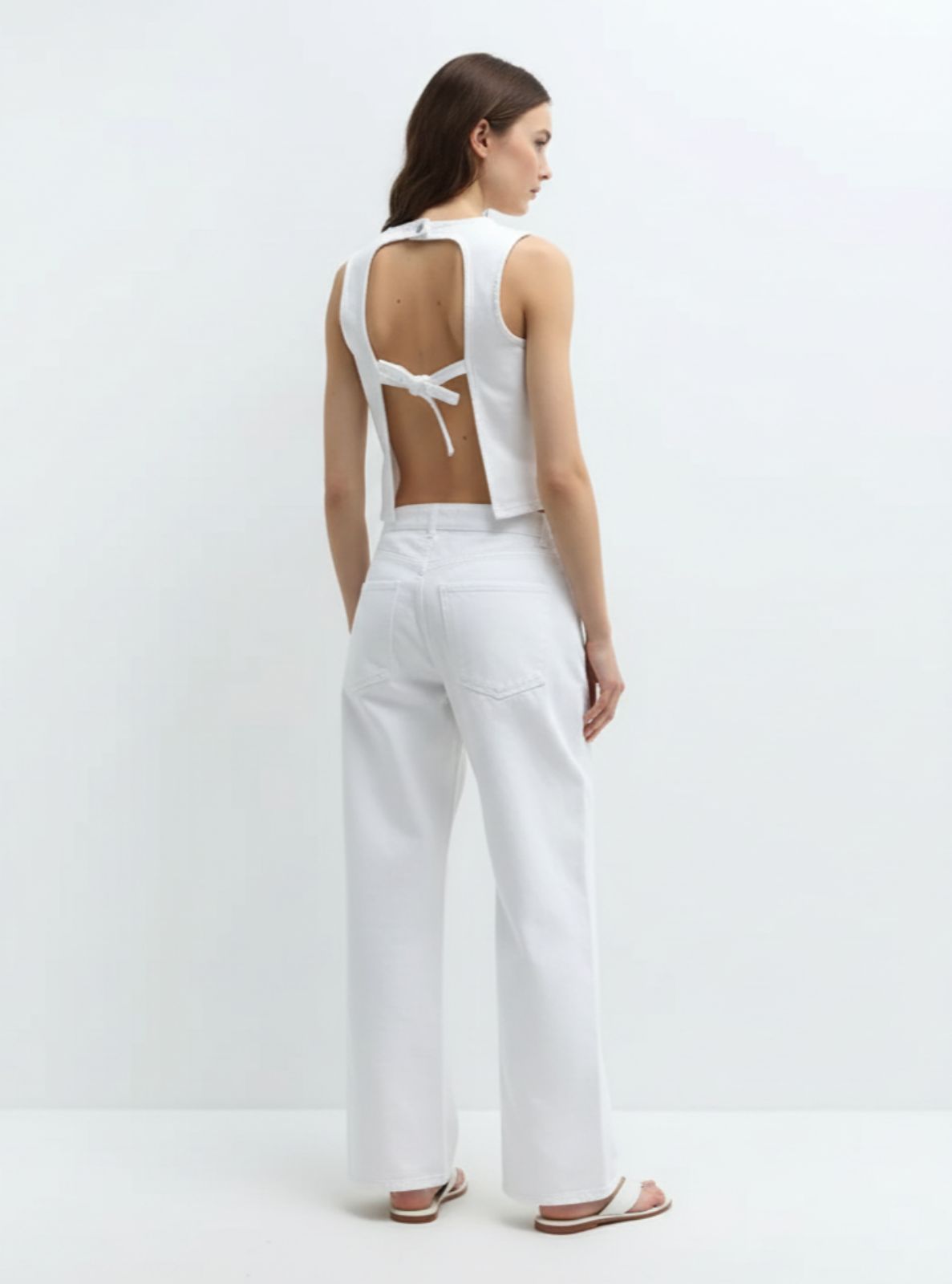 Woman wearing a white sleeveless top and pants on a light gray background