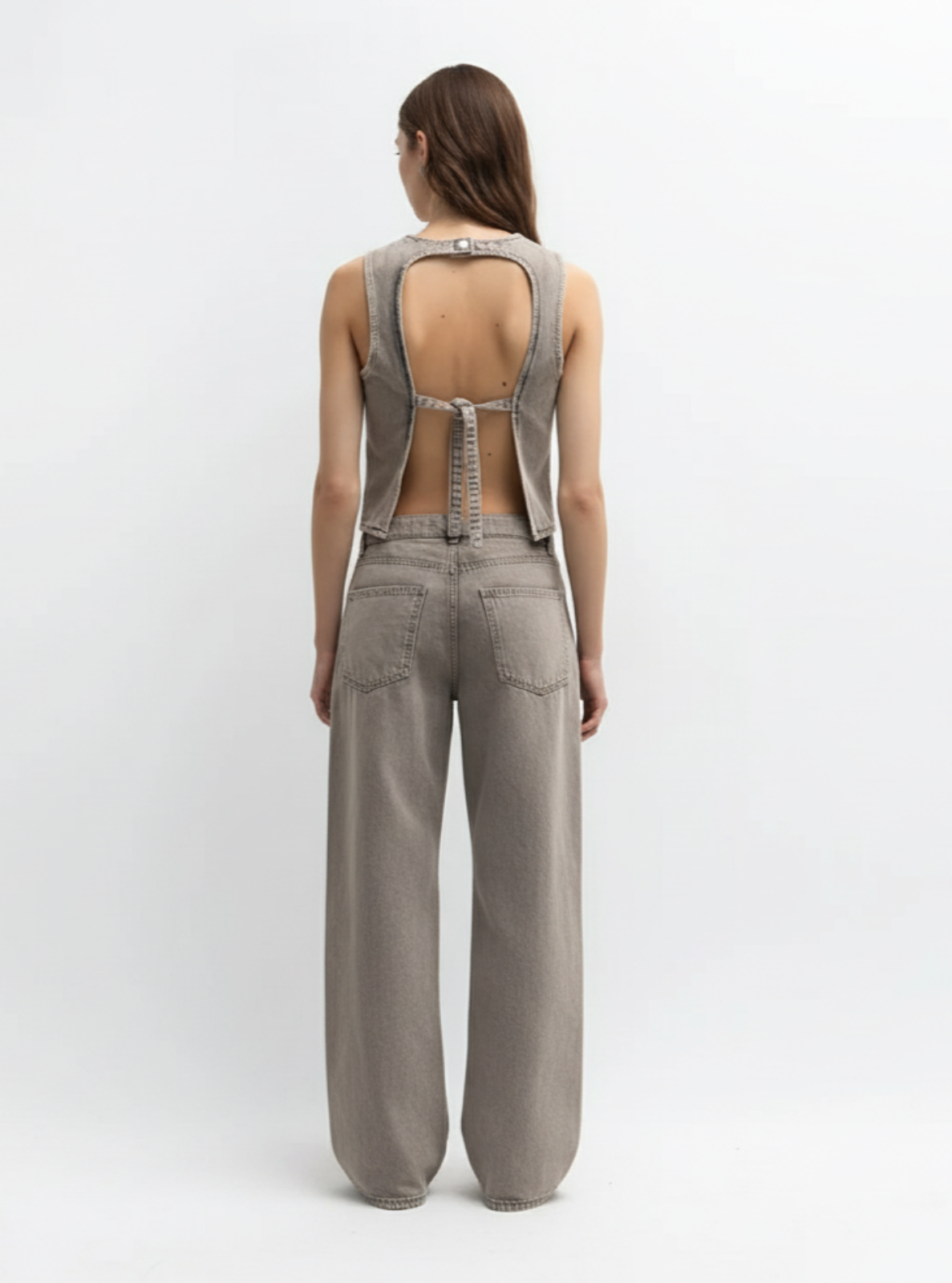 Woman wearing a gray jumpsuit with open back on a white background