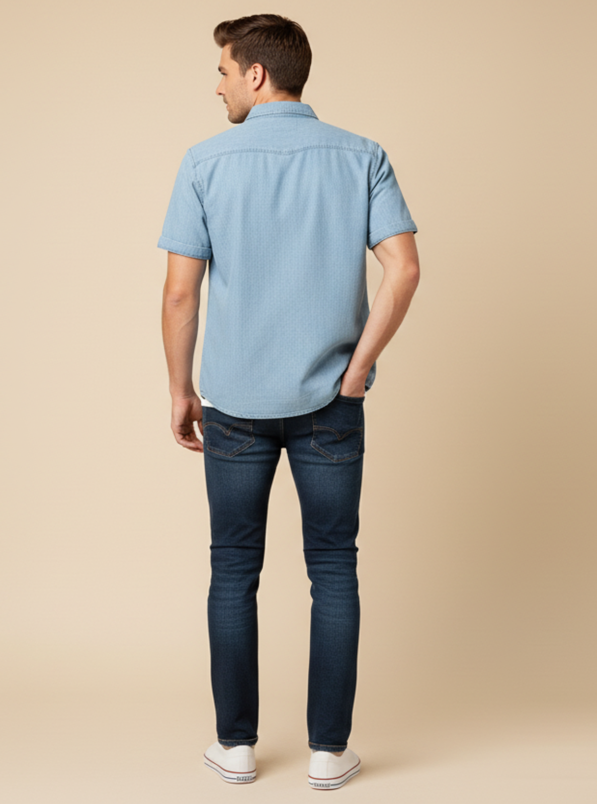 Man wearing a light blue shirt and dark jeans on a beige background