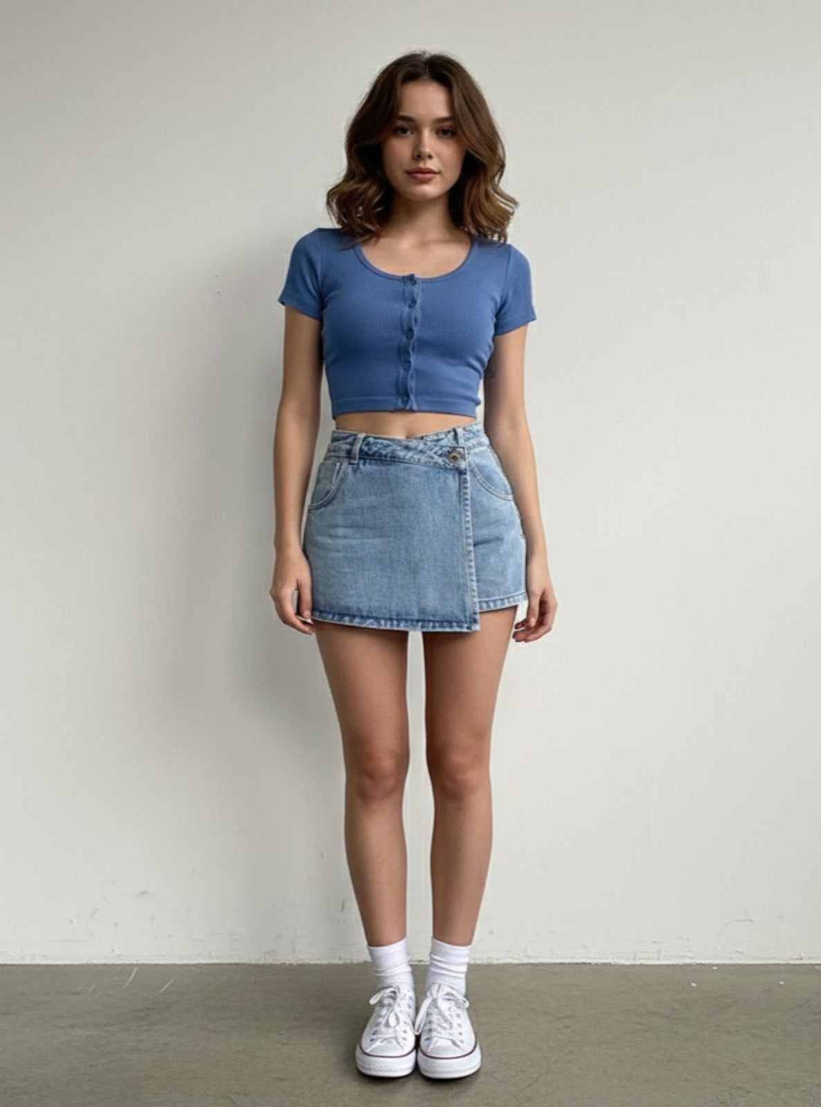 Woman wearing a blue crop top and denim skirt against a plain background