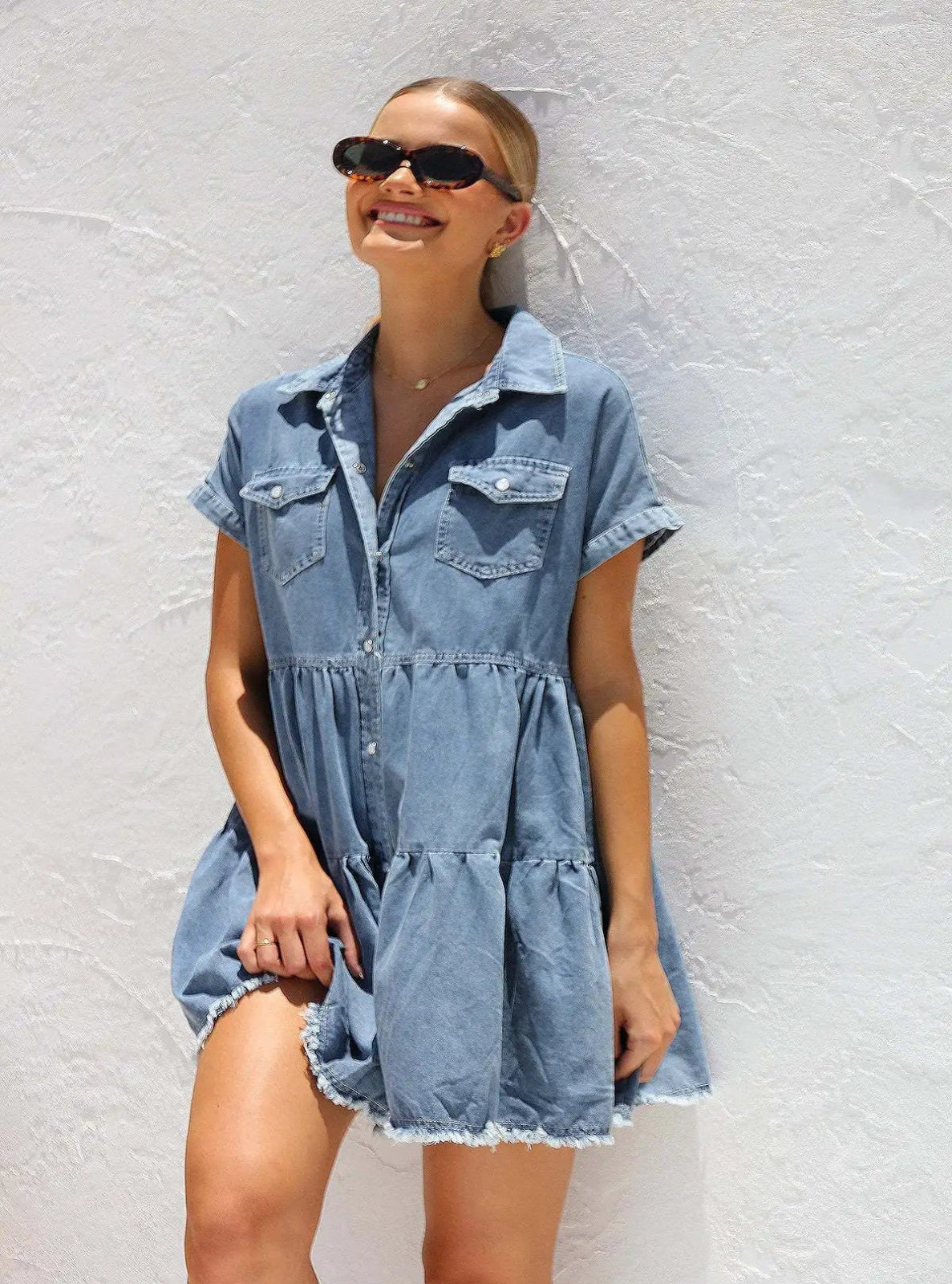 Woman wearing a denim dress against a light gray wall