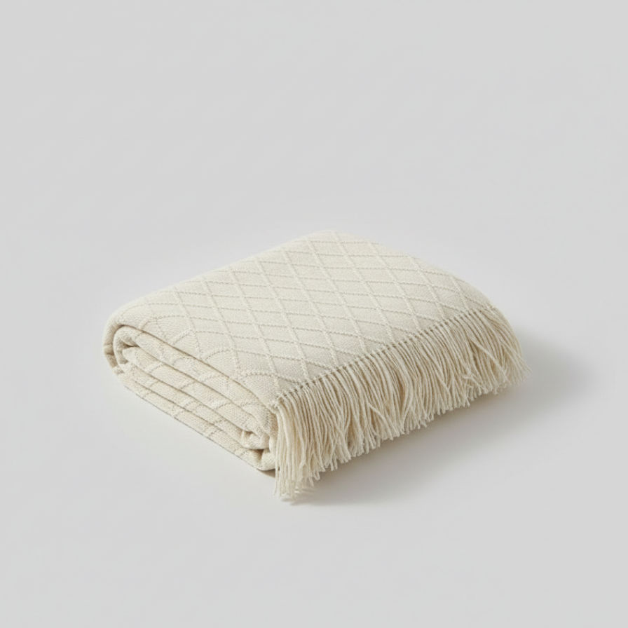Folded cream-colored blanket with fringes on a light gray background