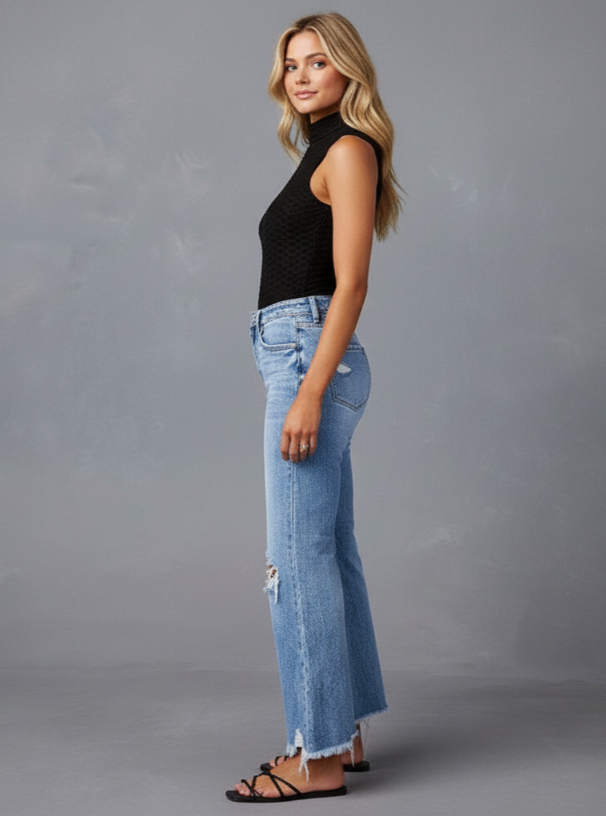 Woman wearing a black sleeveless top and blue jeans against a gray background