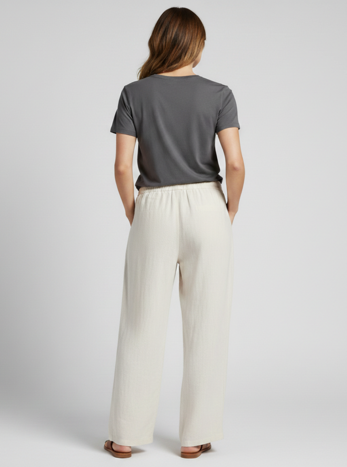 Woman wearing a gray t-shirt and beige wide-leg pants on a light gray background