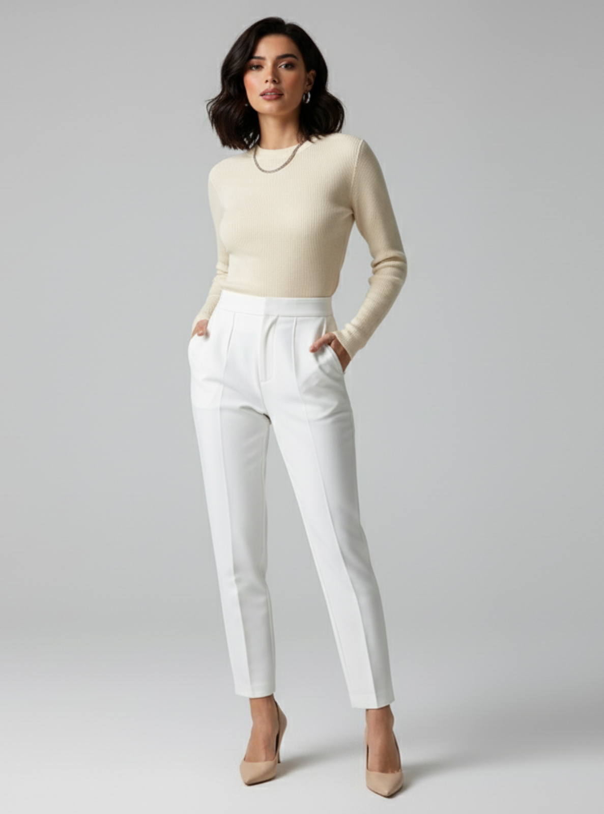 Woman wearing a beige sweater and white pants on a gray background