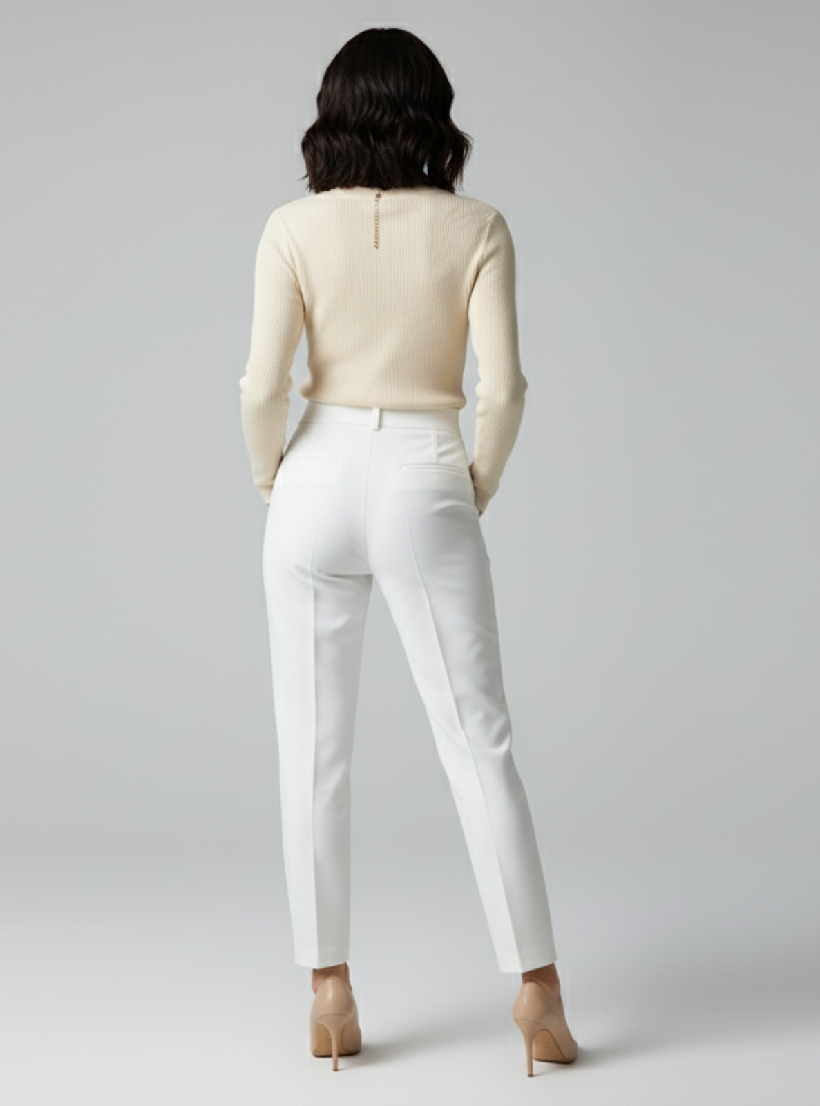 Woman wearing a beige top and white pants on a gray background