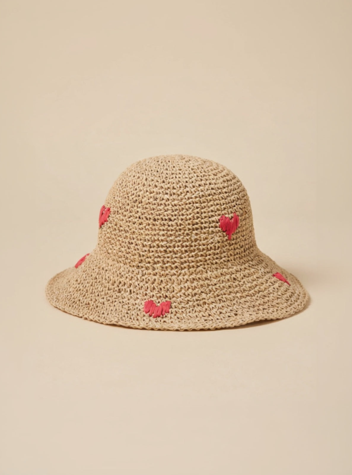 Woven straw hat with pink heart decorations on a beige background