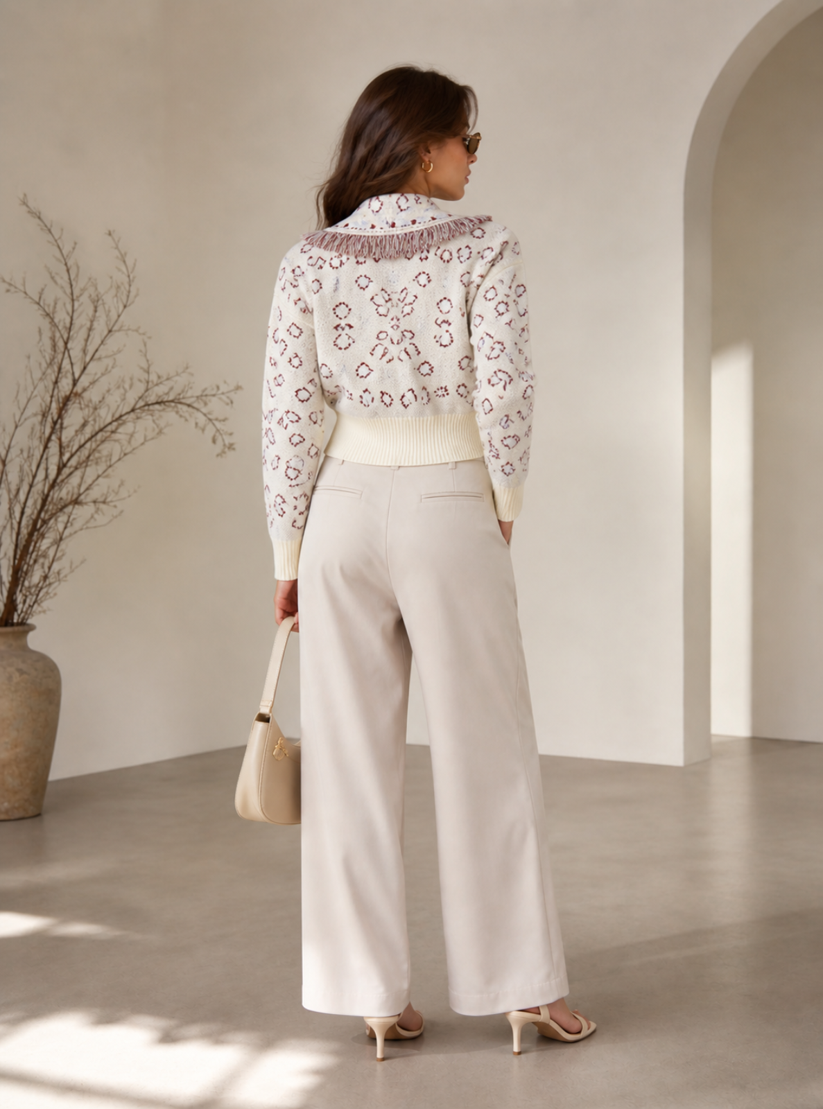 Woman wearing a white blouse with lace details and beige pants in a minimalistic room.