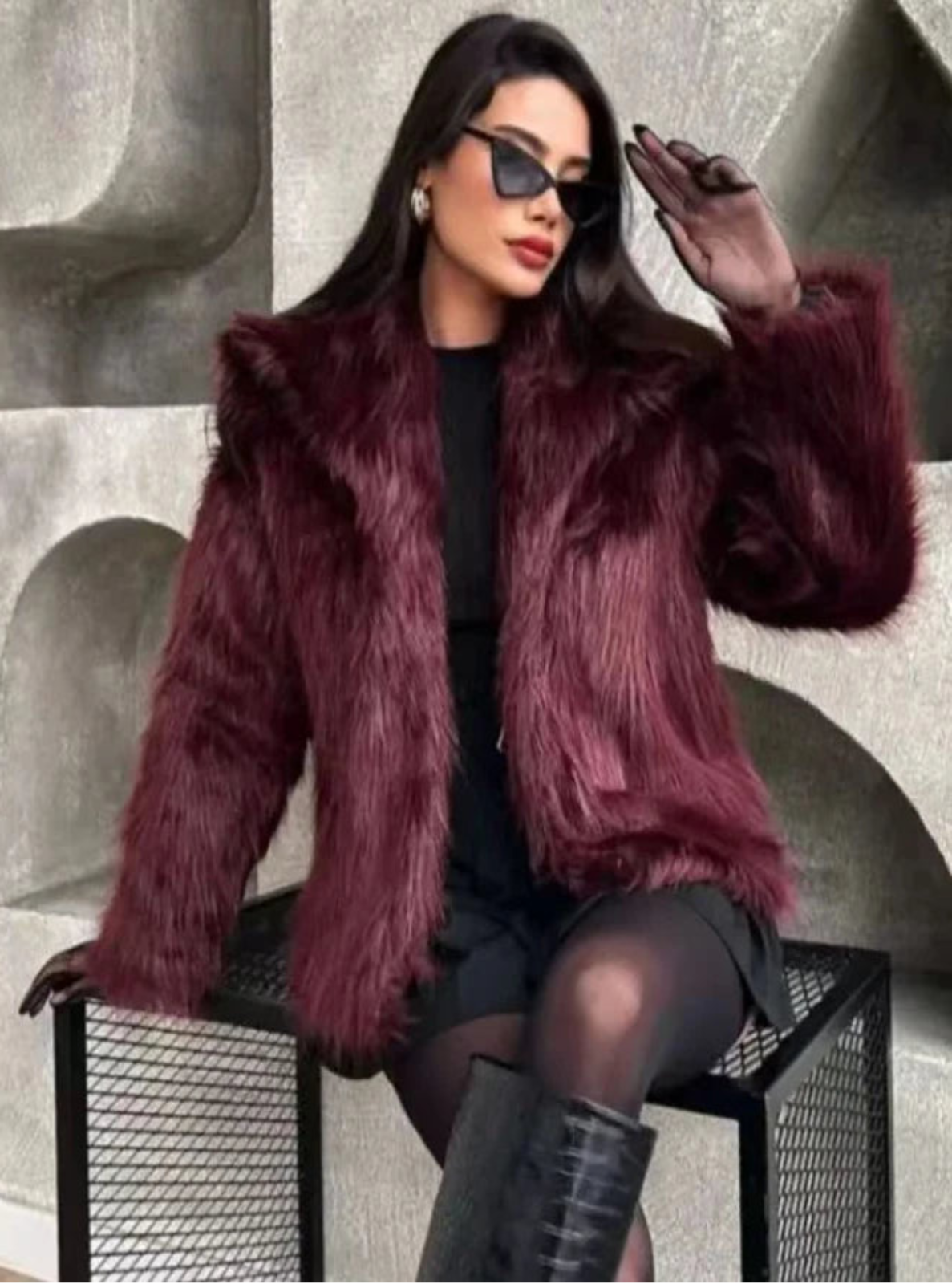 Woman wearing a purple fur coat and black sunglasses against a textured wall.