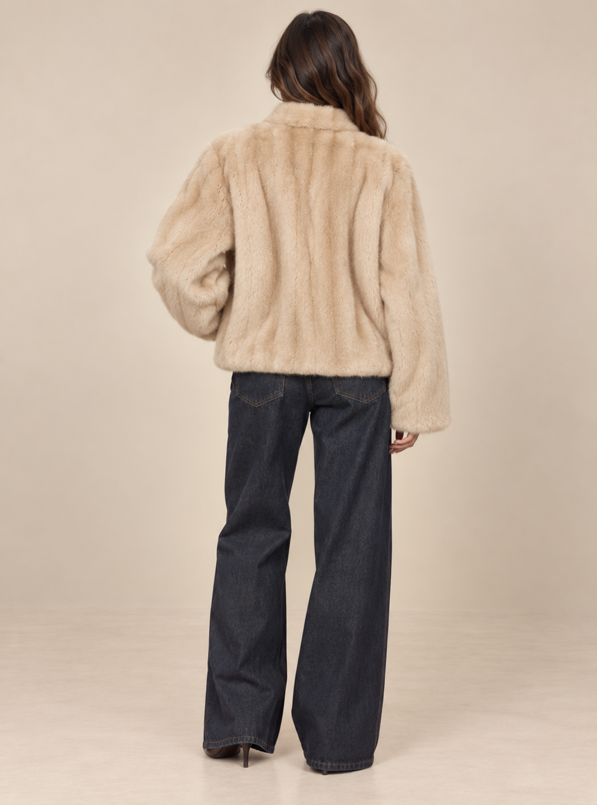 A model shown from the back wearing a beige faux fur cropped jacket and dark blue wide-leg jeans against a solid beige studio background.