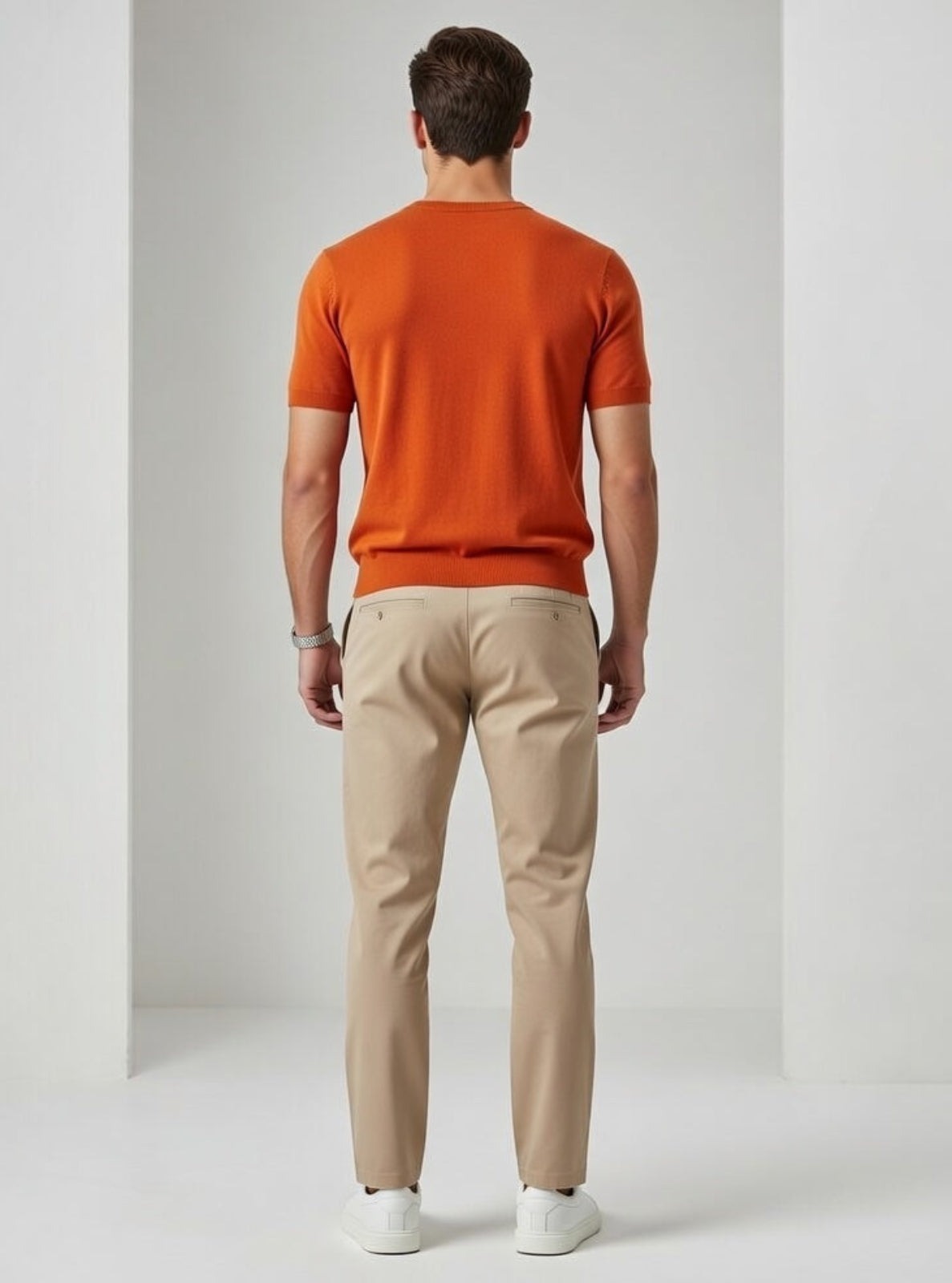 Man wearing an orange shirt and beige pants against a white background