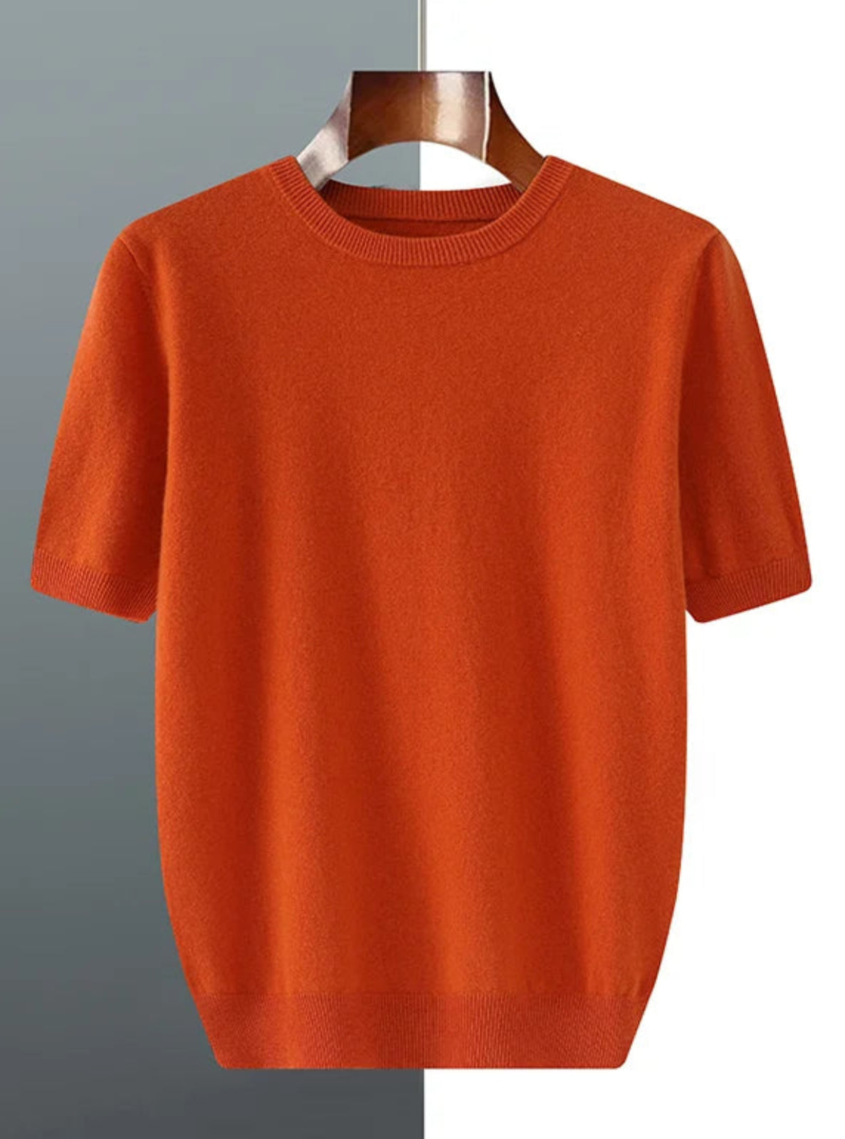 Orange sweater on a hanger against a gray and white background