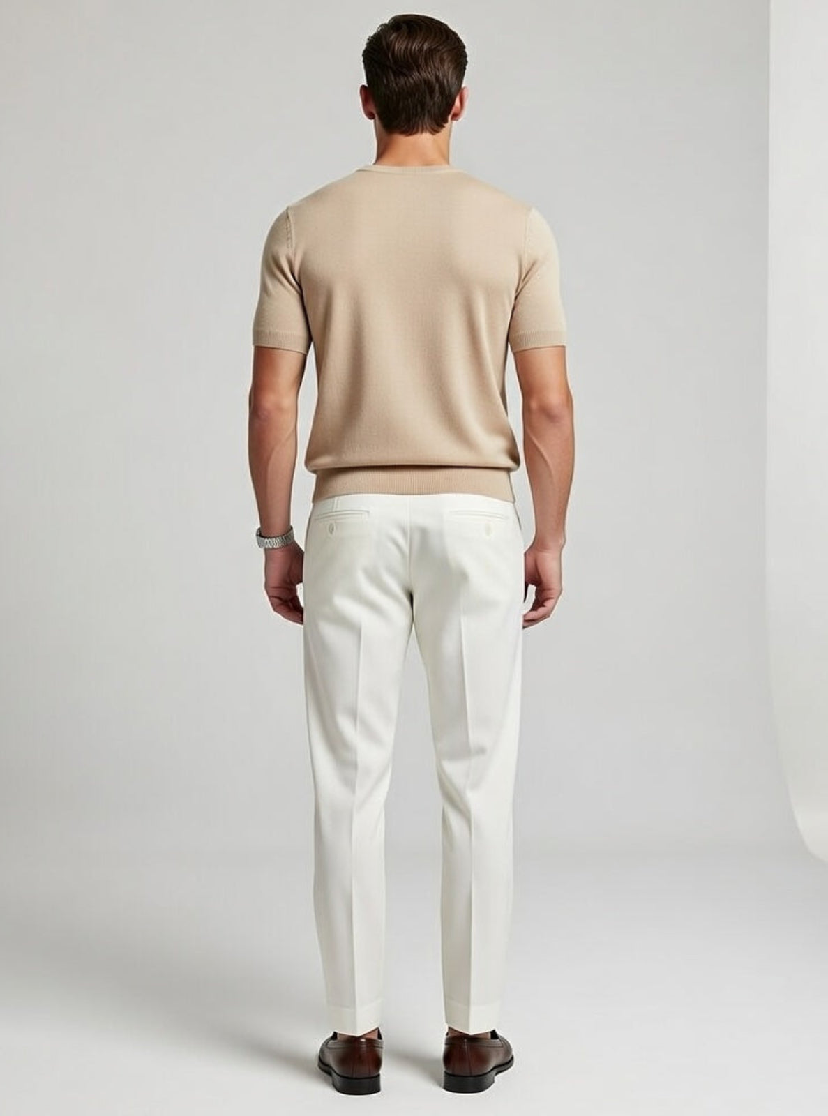 Man wearing a beige sweater and white pants against a plain background