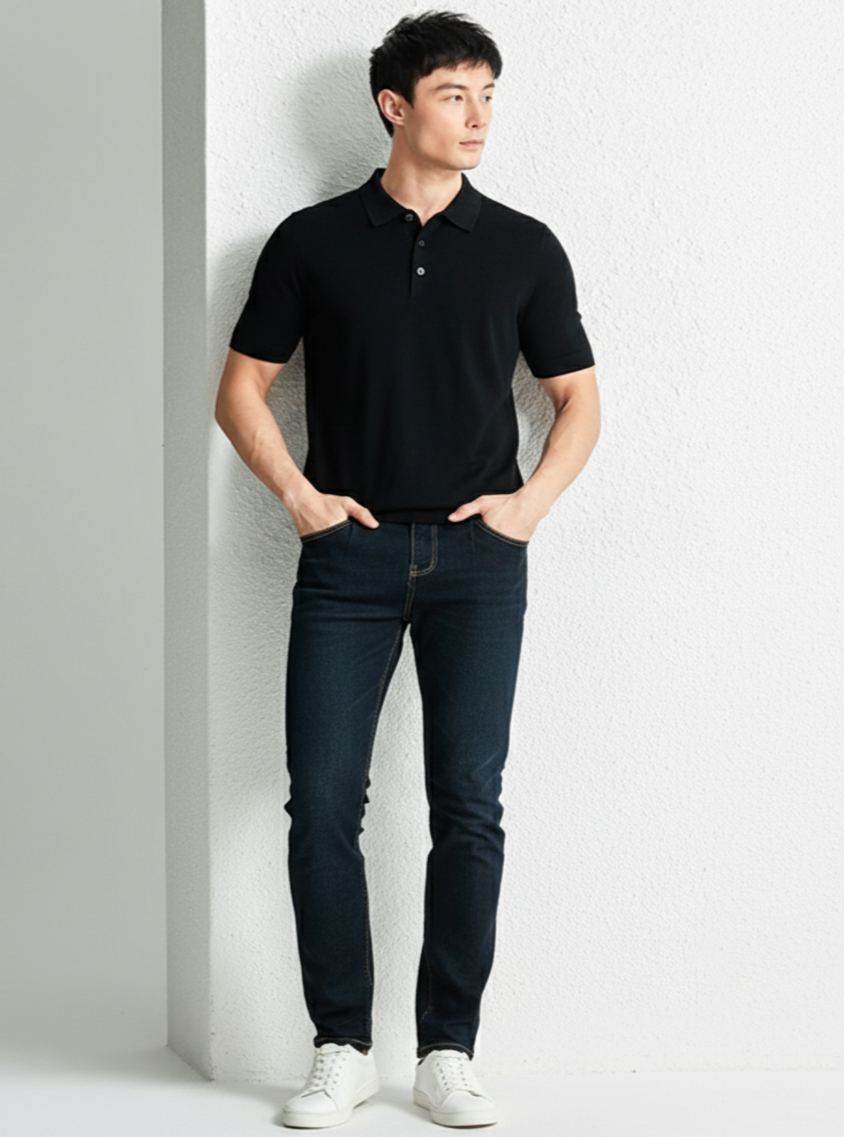 Man wearing a black polo shirt and dark jeans against a light gray background