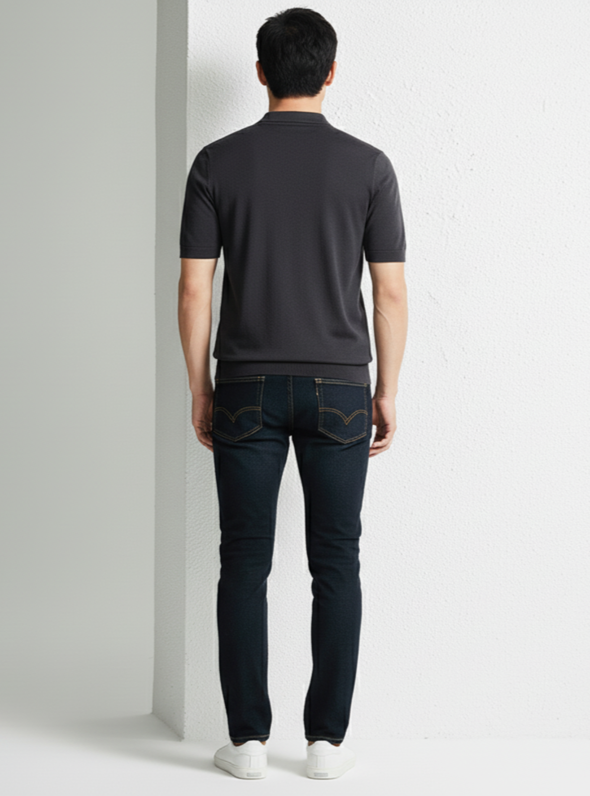 Man wearing a dark gray polo shirt and black jeans against a white background