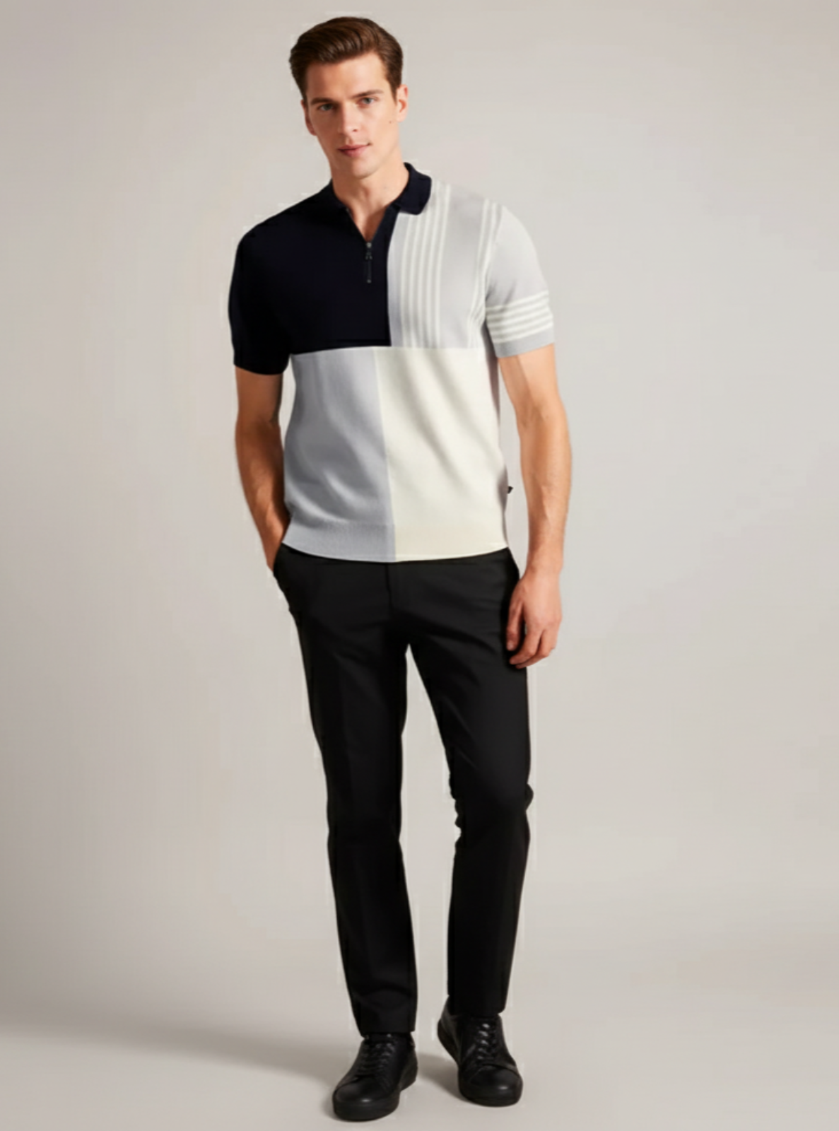 Man wearing a black, white, and gray color-blocked polo shirt with black pants on a plain background