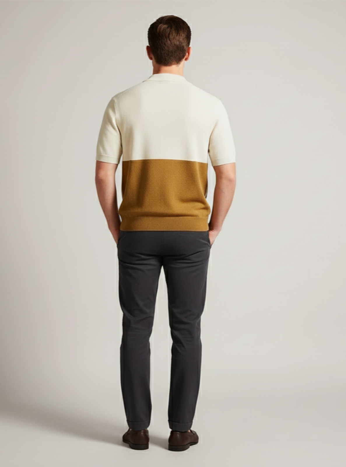 Man wearing a two-tone sweater and dark pants on a plain background
