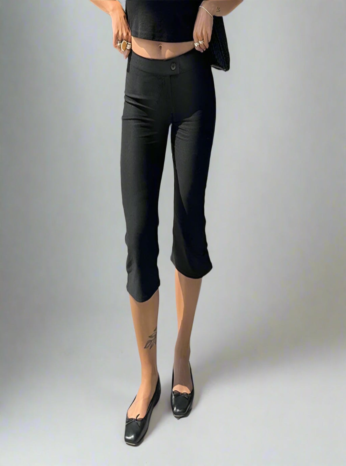 Person wearing black capri pants and black shoes on a white background