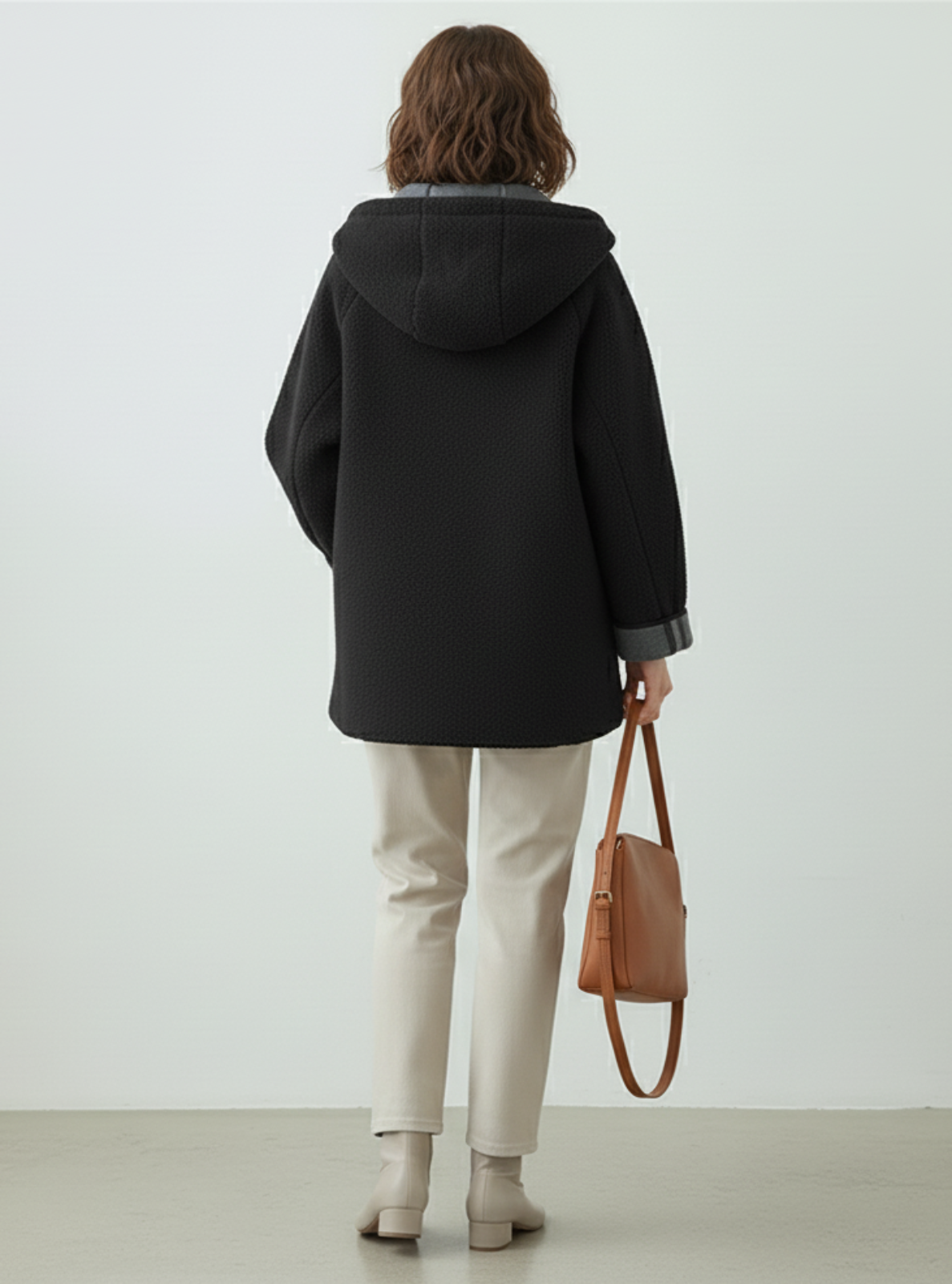 Person wearing a black coat holding a brown bag against a white background
